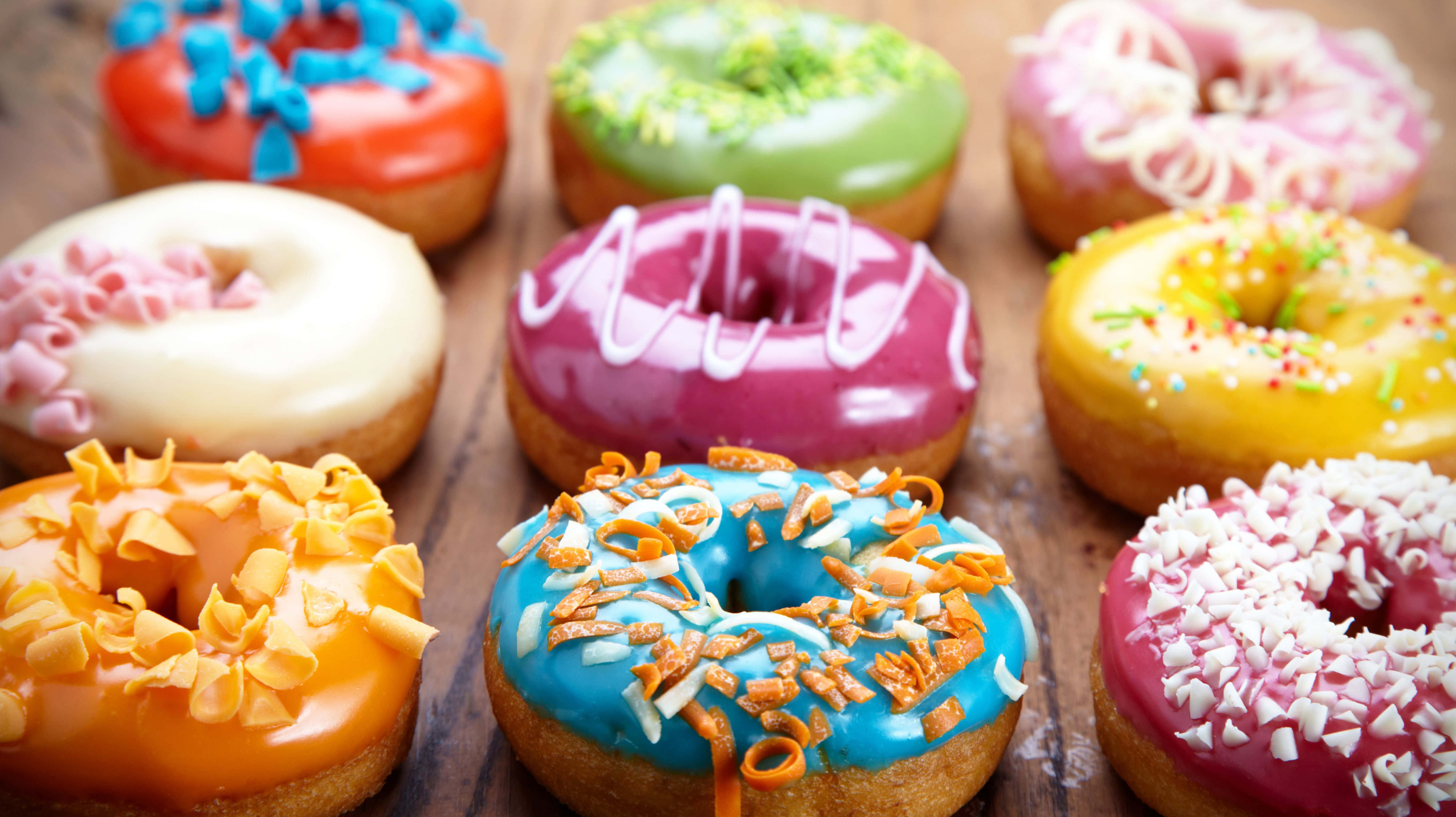 donuts 桌布 壁紙 — 色彩繽紛的釉面冬甩，上面有彩色配料，擺放在質樸的木質表面上。
