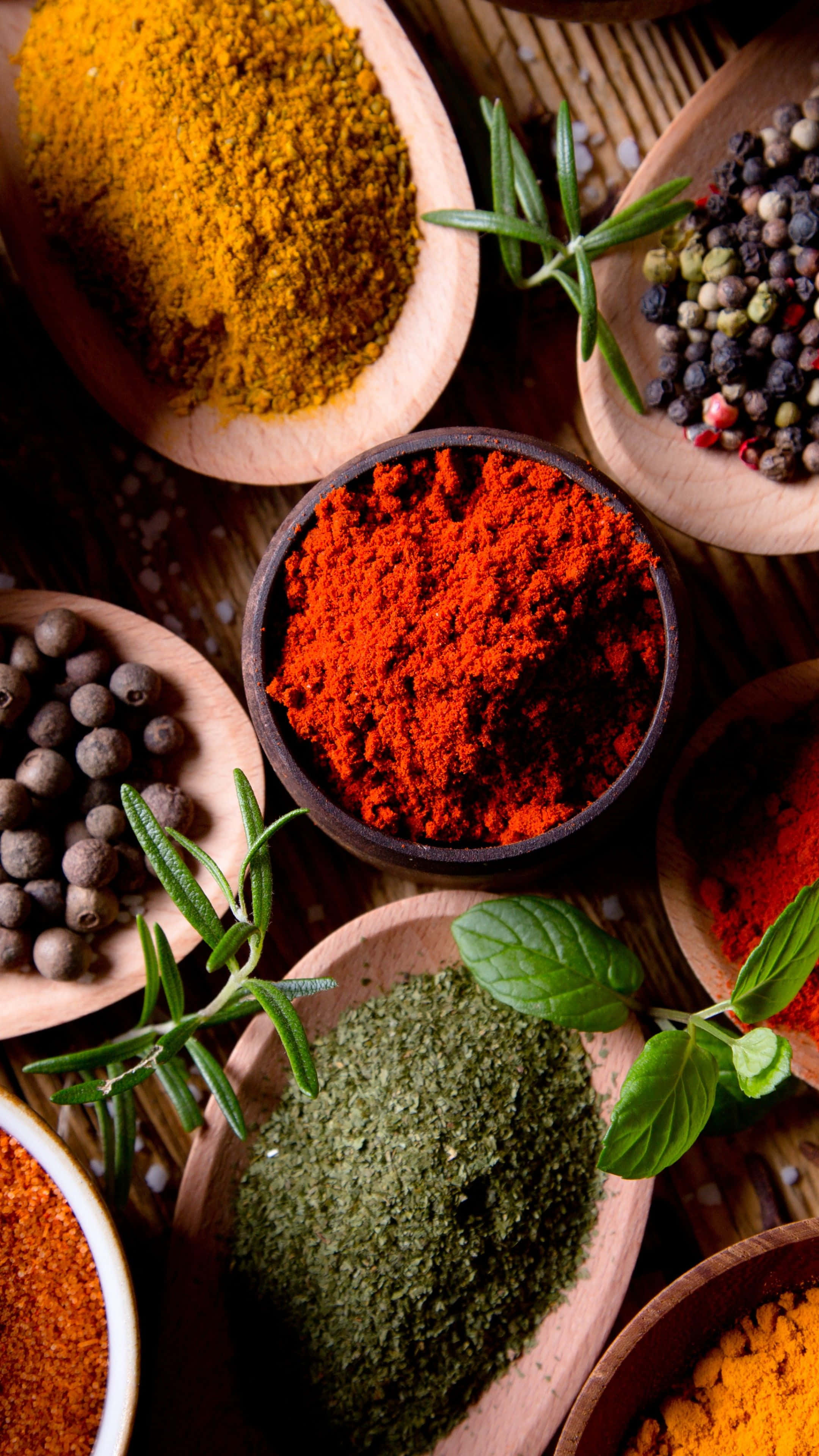 Spice 桌布 壁紙 — 色彩繽紛的香料和新鮮香草放在木碗中，排列在有紋理的表面上。