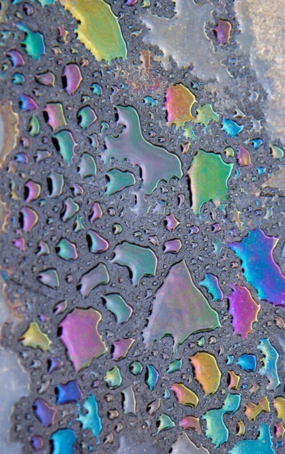 色彩美學：玻璃上的雨滴 壁紙 — 特寫鏡頭：水面上虹彩油膜在深色紋理表面上形成鮮豔彩虹圖案。