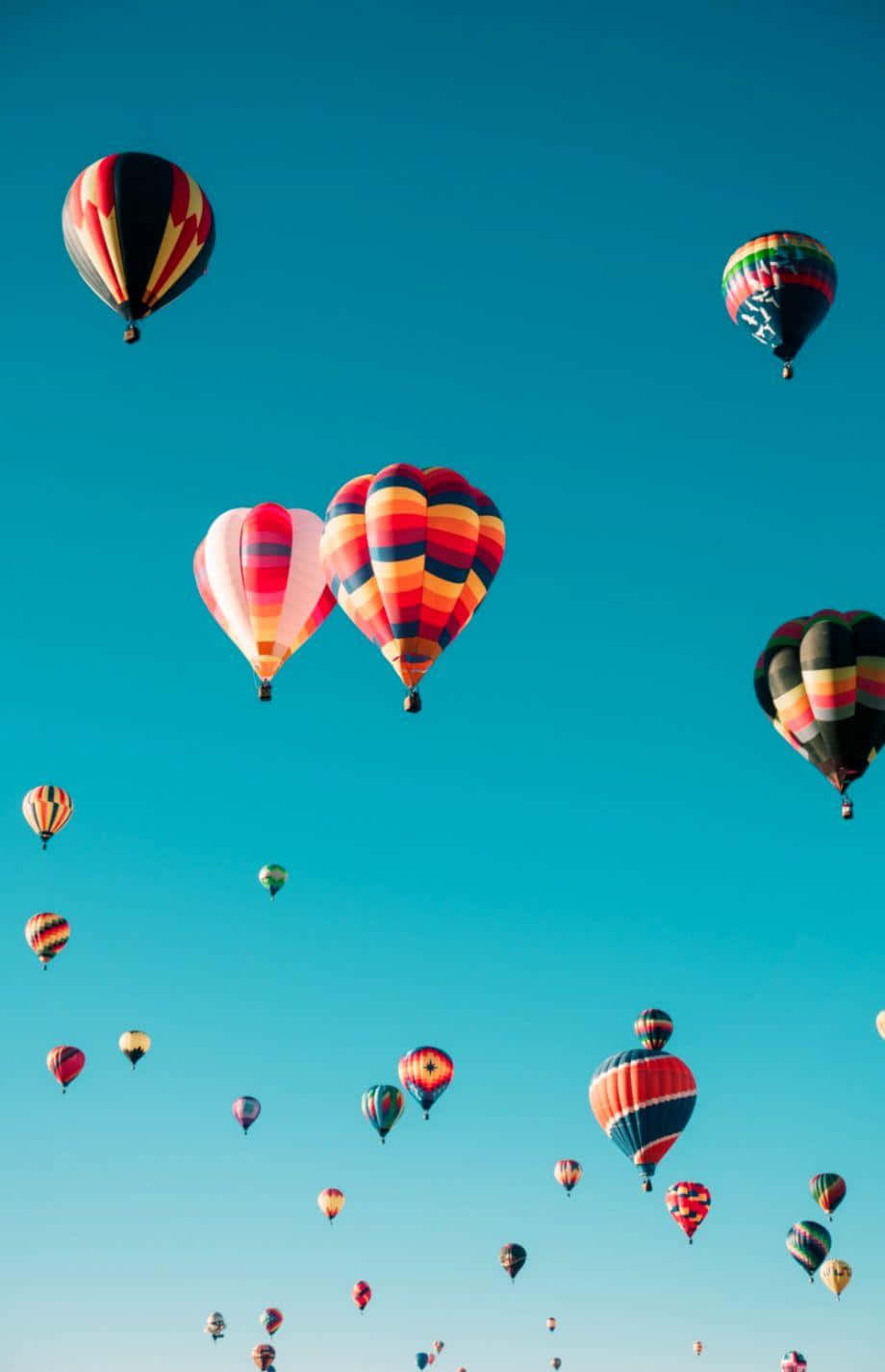 Balloon 桌布 壁紙 — 色彩鮮豔、圖案大膽的熱氣球在晴朗的碧藍天空中飄移，形成一場節日般的空中聚會。