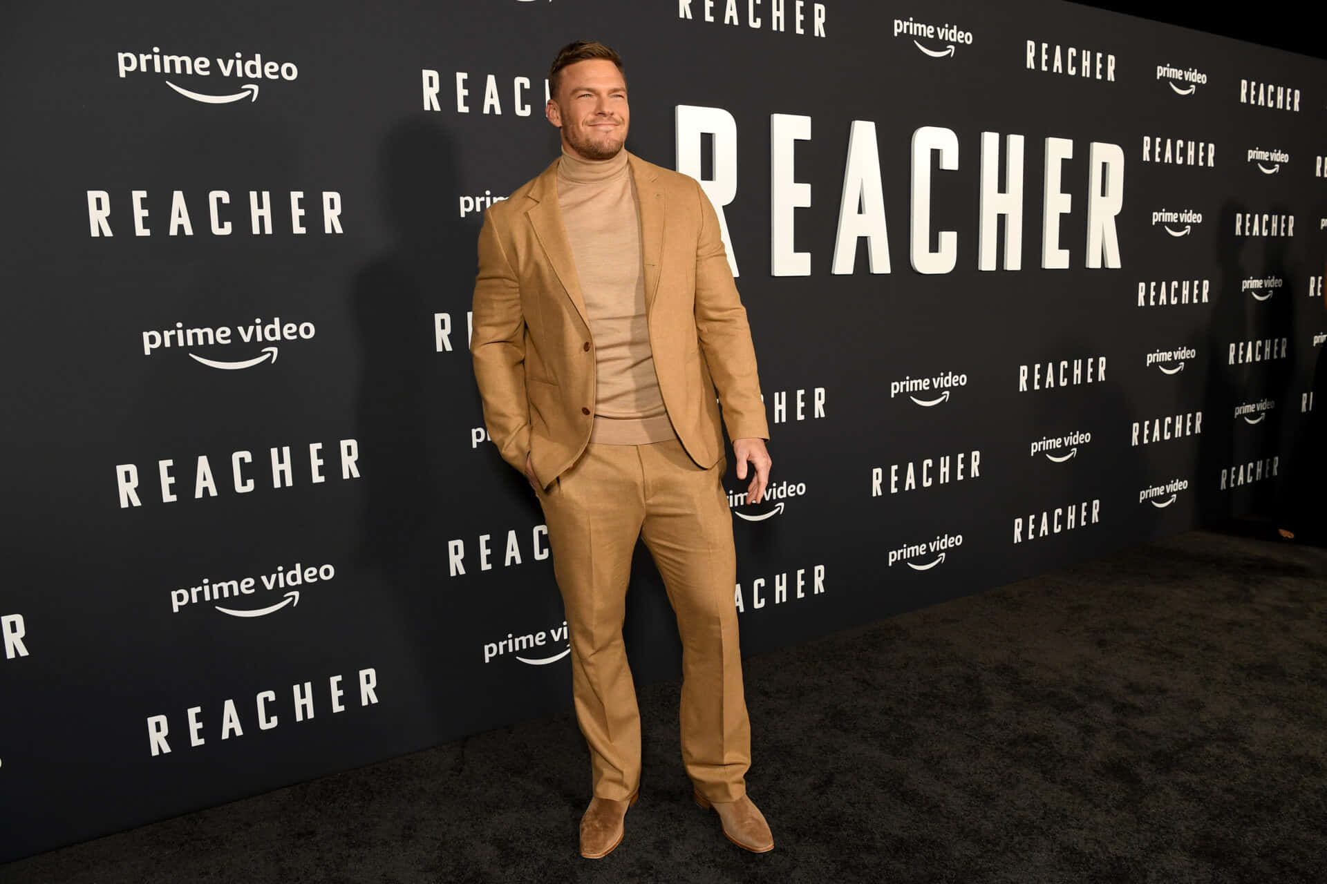身穿米色西裝的男子在Reacher首映活動的黑色地毯上。