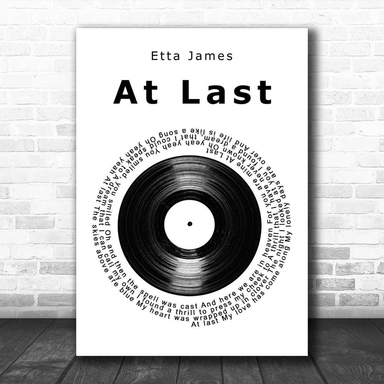 艾塔·詹姆斯《At Last》錄音室專輯海報 壁紙 — Etta James《At Last》嘅極簡黑白海報，歌詞圍繞黑膠唱片形成圓圈，掛喺白色磚牆上，下面係深色木地板。