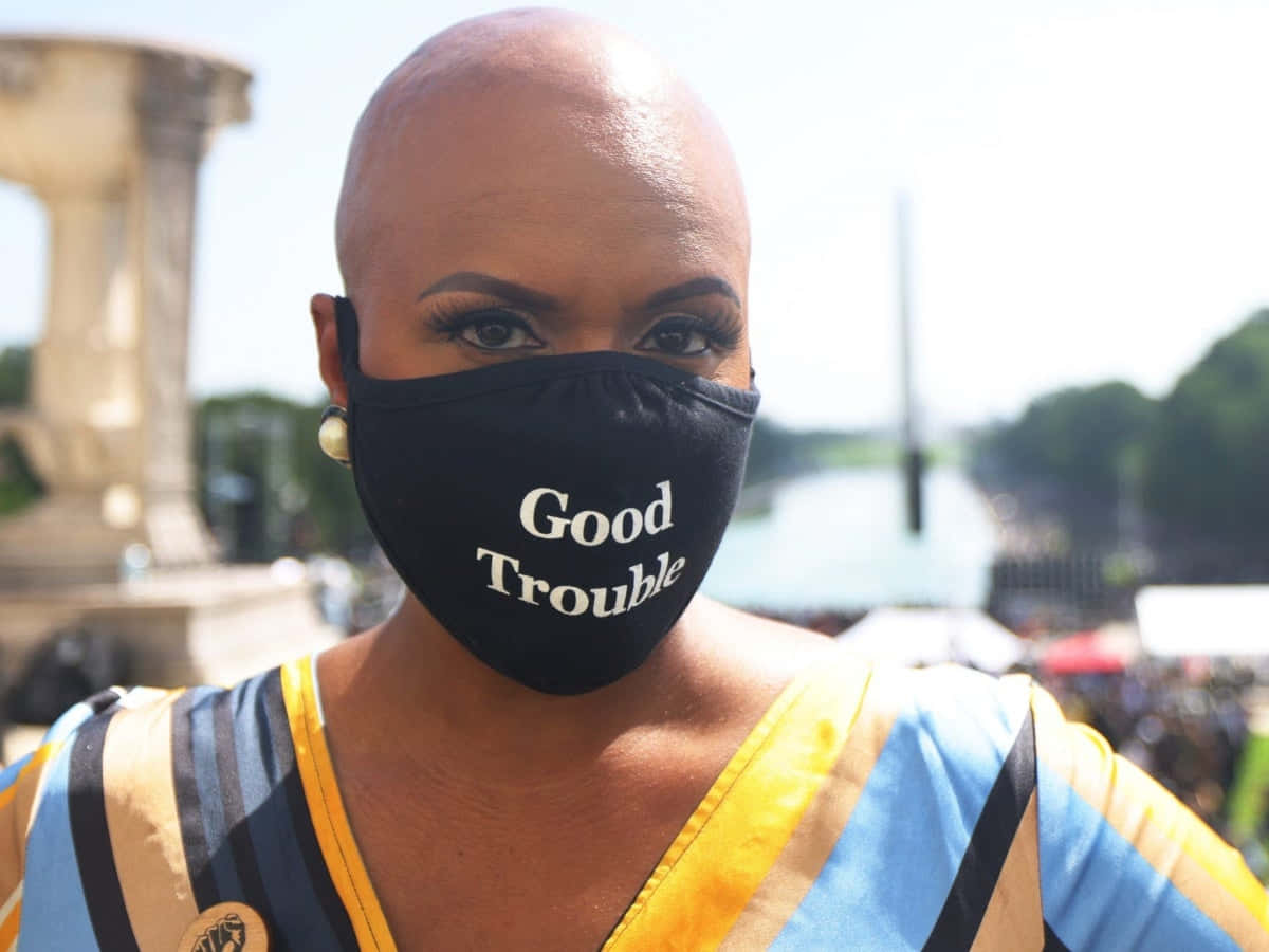 一位在陽光明媚的城市環境中佩戴「Good Trouble」口罩的女性。
