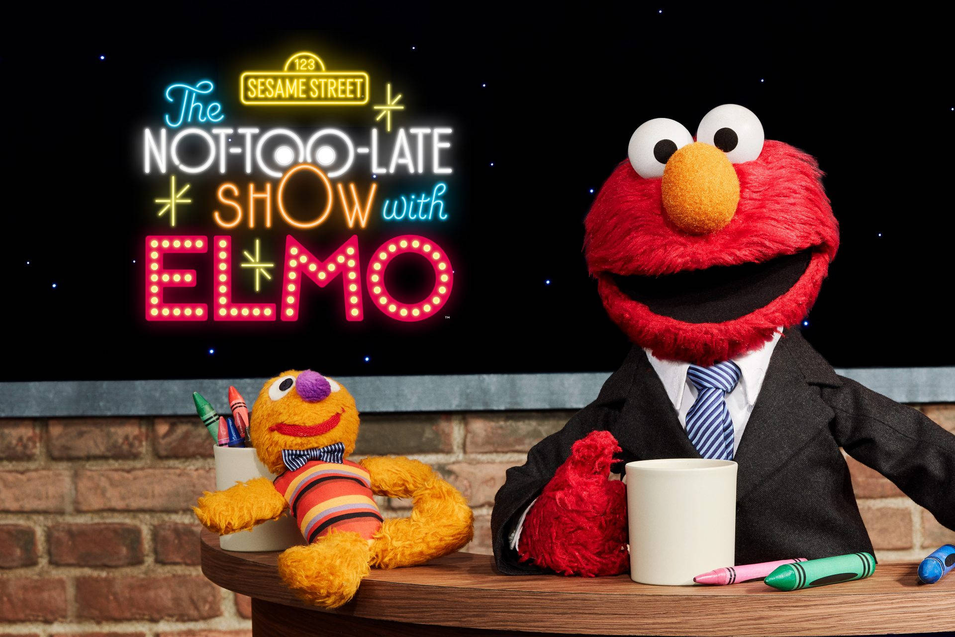 Elmo 身穿西裝主持深夜節目，磚牆佈景中有一位黃色木偶嘉賓。