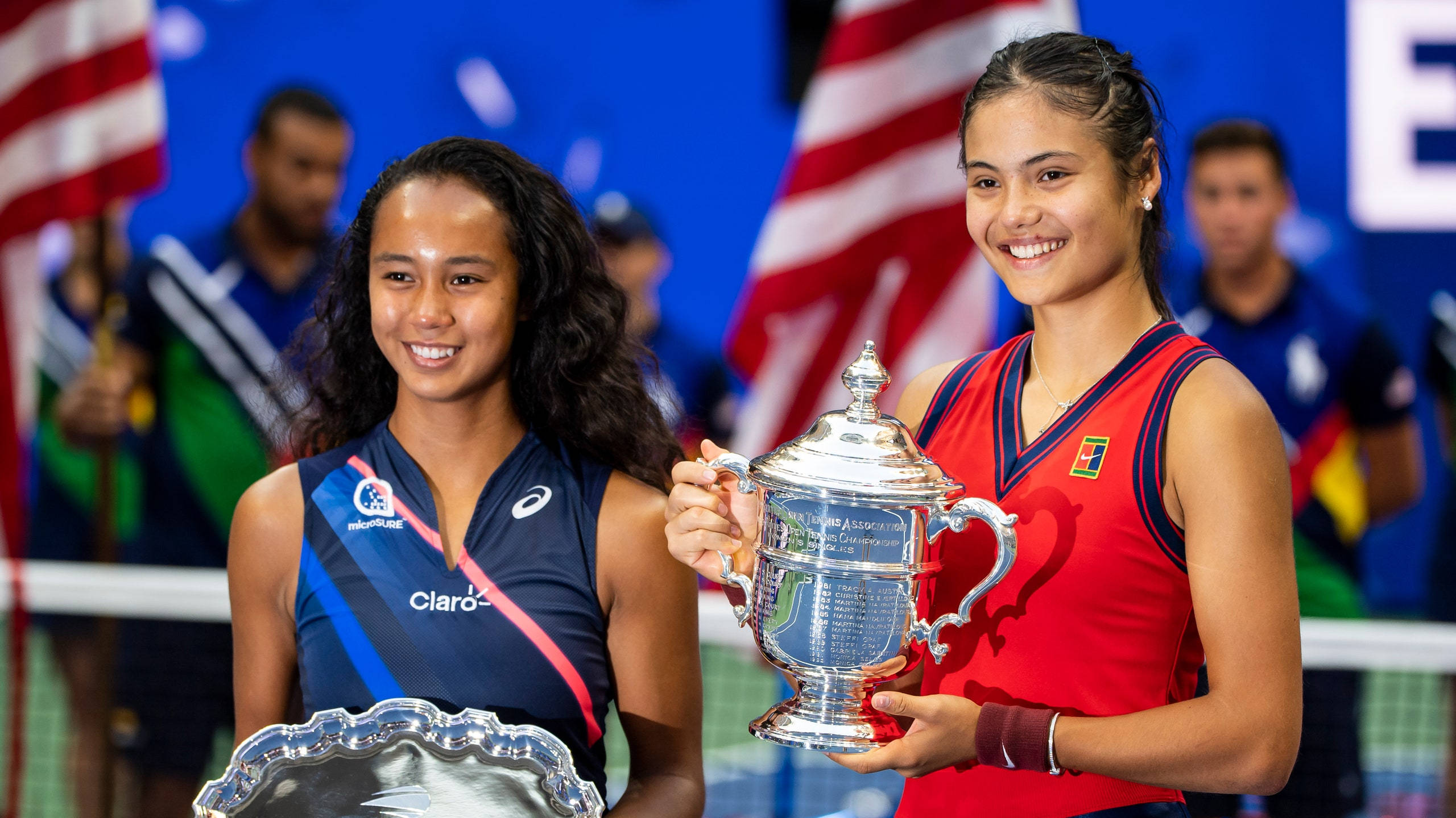 艾瑪·拉杜卡努與獎盃合影 壁紙 — 兩位微笑的女性網球選手站在球場上，手持獎盃，身後有美國國旗。