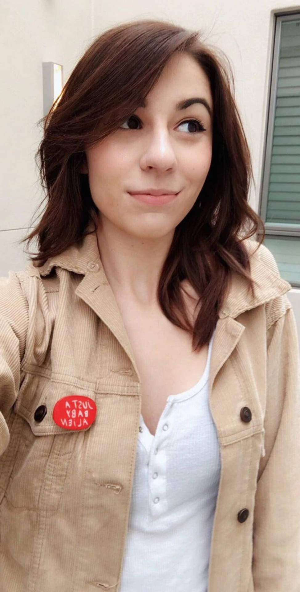 年輕女性穿著米色外套，戴著紅色外星人別針，微笑著看向別處。