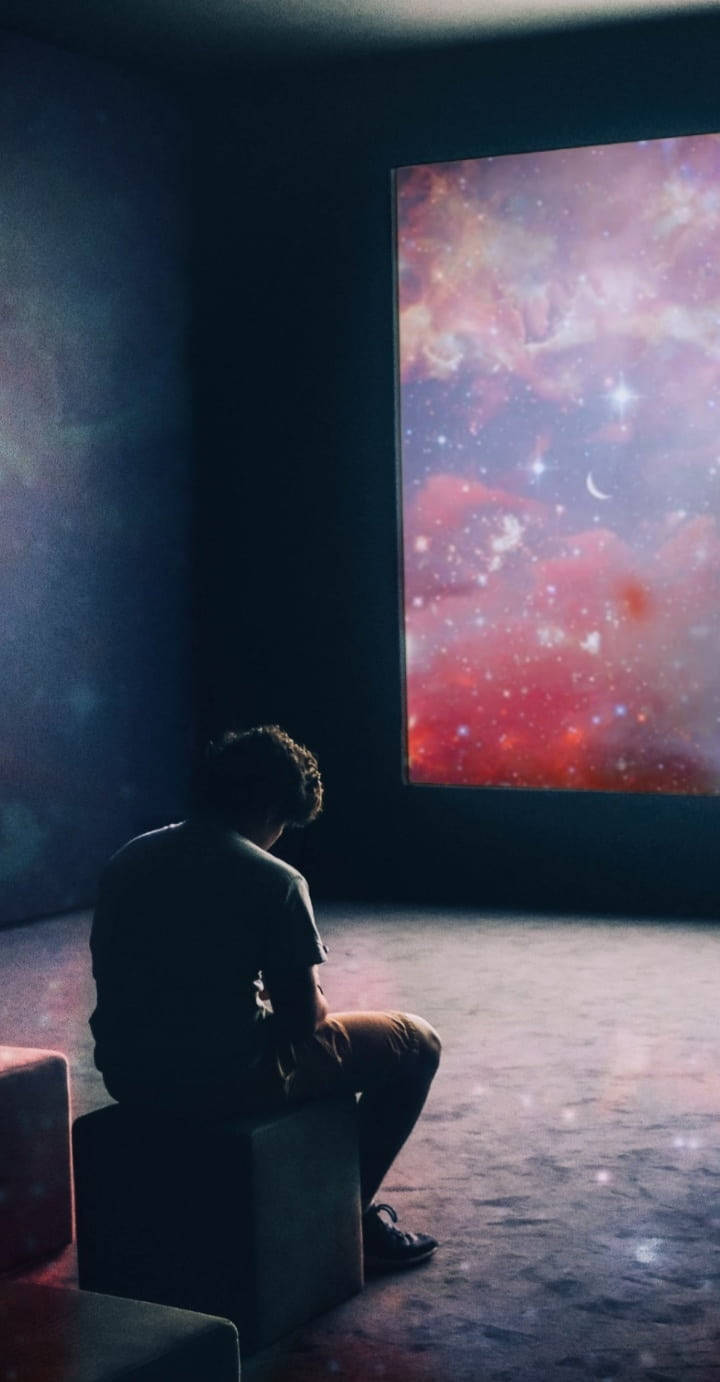一個人坐在黑暗的房間裡觀看宇宙星場投影。
