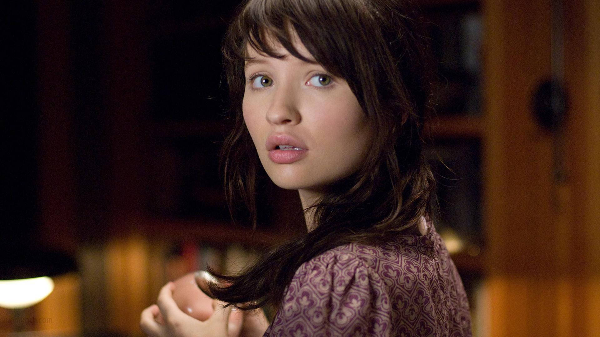 艾米莉·布朗寧飾演《The Uninvited》中的Anna Ivers（2009） 壁紙 — 一位棕色頭髮的年輕女性在溫暖的室內環境中回頭看，眼睛睜得大大的。