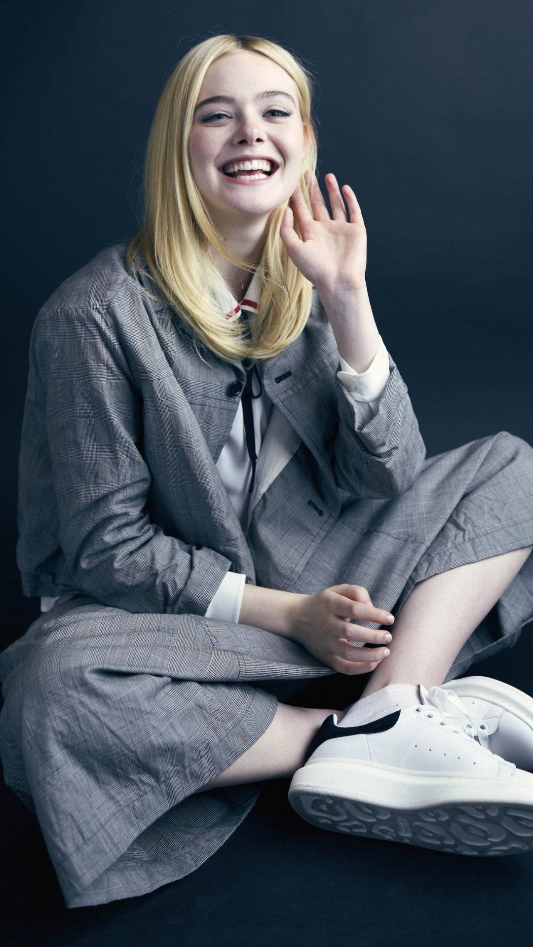 金髮年輕女性穿著灰色西裝和白色運動鞋微笑揮手。