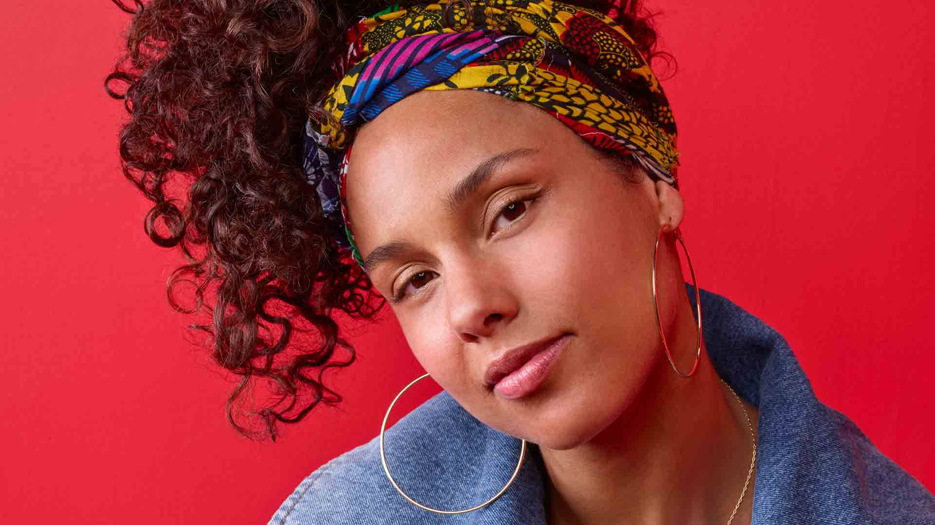 艾莉西亞·凱斯佩戴髮帶 壁紙 — 一位擁有捲曲頭髮和彩色頭巾的女性，在鮮豔的紅色背景下溫柔凝視。