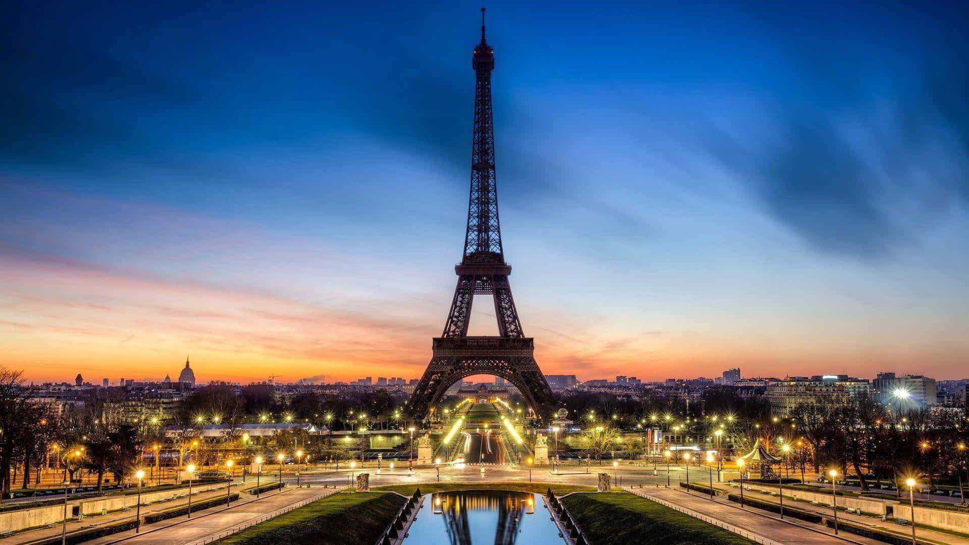 Eiffel Tower 桌布 壁紙 — 艾菲爾鐵塔在暮色天空下高聳矗立，溫暖的城市燈光映照在中央水道中。