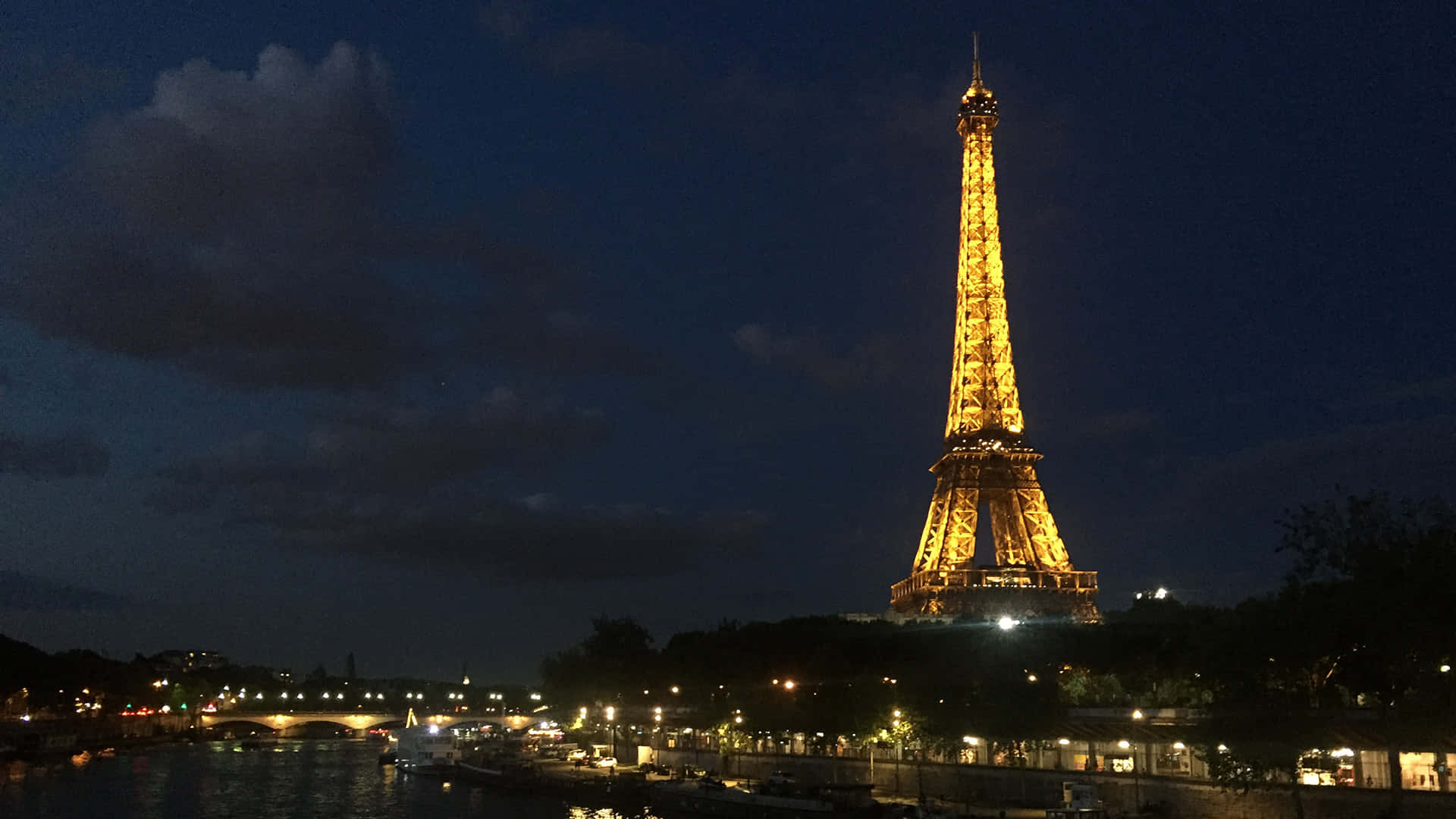 french 桌布 壁紙 — 艾菲爾鐵塔在深藍色夜空下溫暖地發光，燈光倒映在下面的塞納河上。