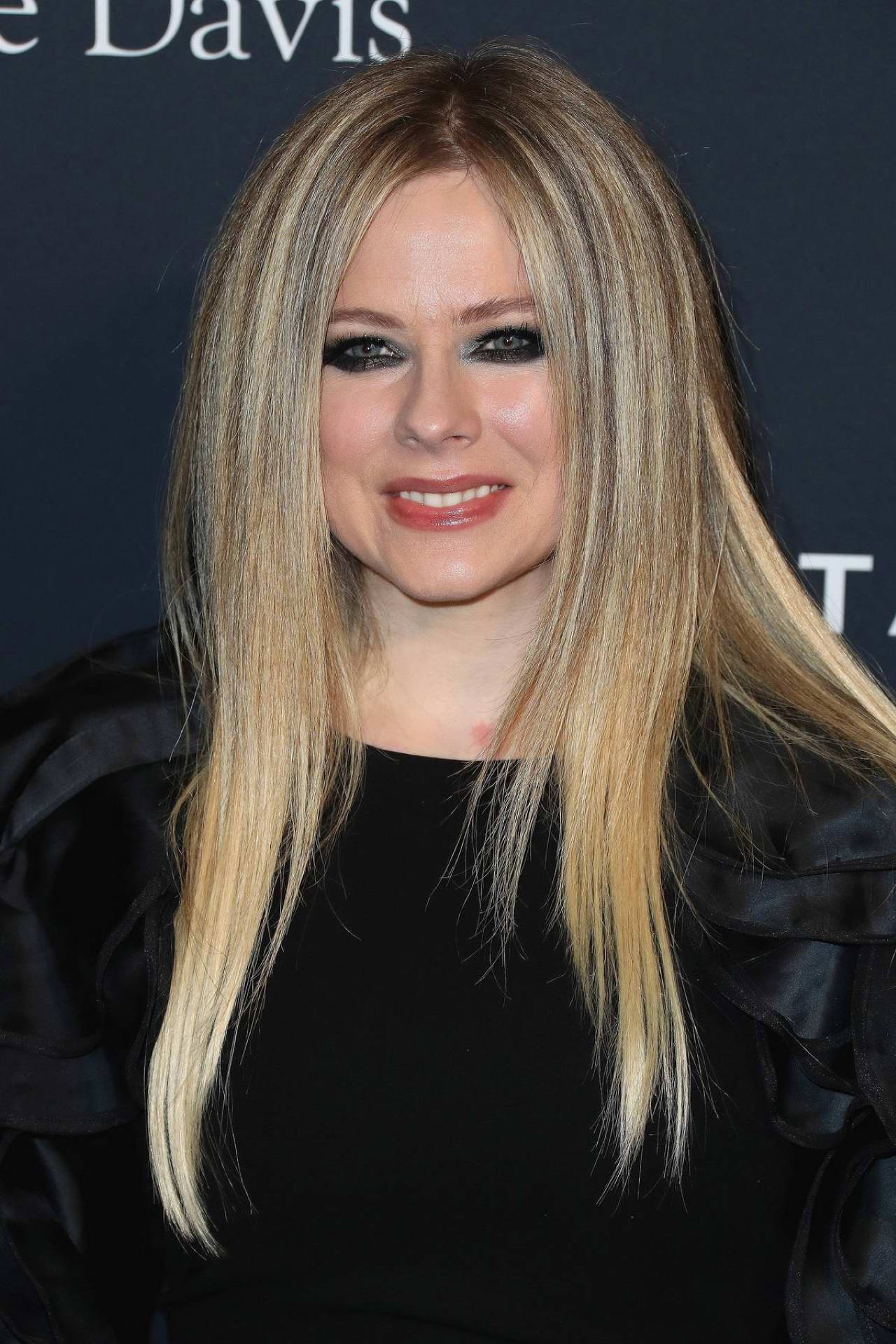 Avril Lavigne 在活動中穿著黑色服裝，金色頭髮，大膽妝容。