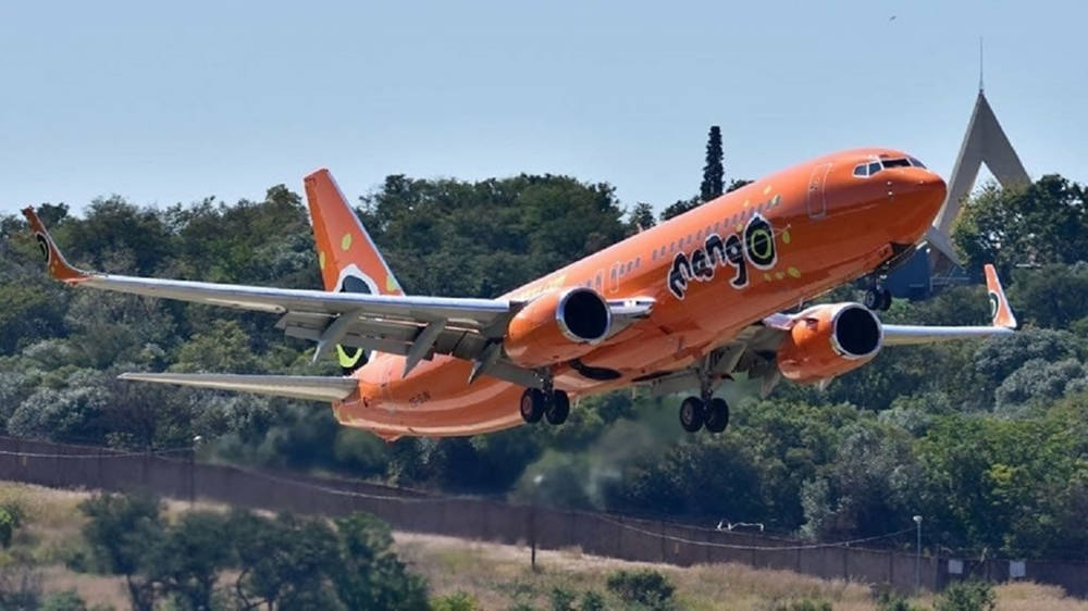 橙色Mango Airlines噴射機從被樹木環繞的跑道上升。