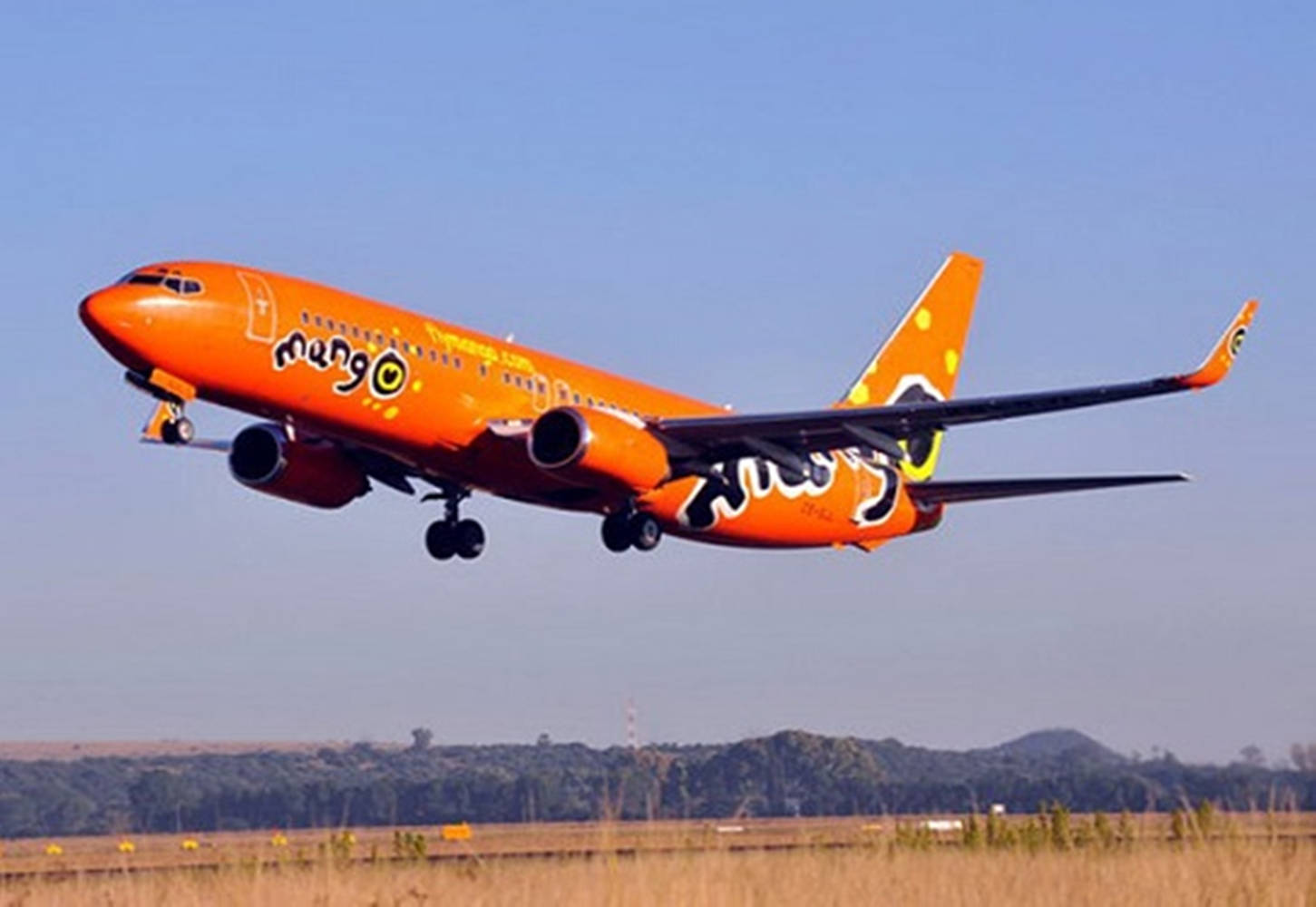 橙色Mango Airlines噴射機從跑道上升，背景有綠色山丘。