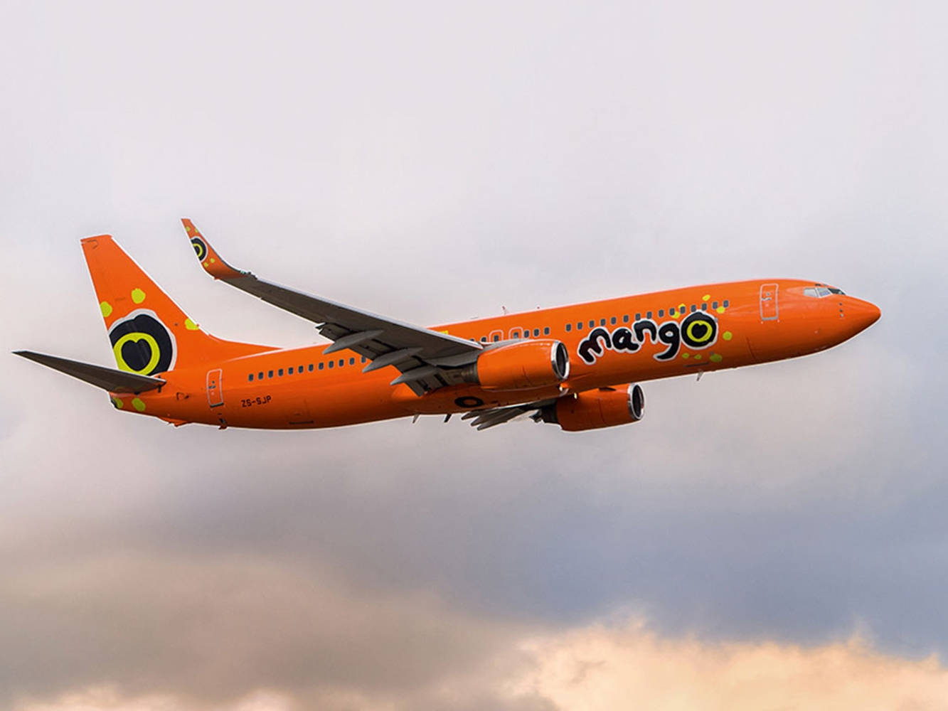橙色Mango Airlines飛機在多雲的夕陽天空下飛行。