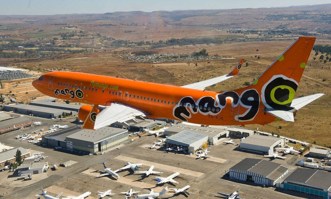 橙色芒果航空貨機飛越機場機庫和停放的飛機。