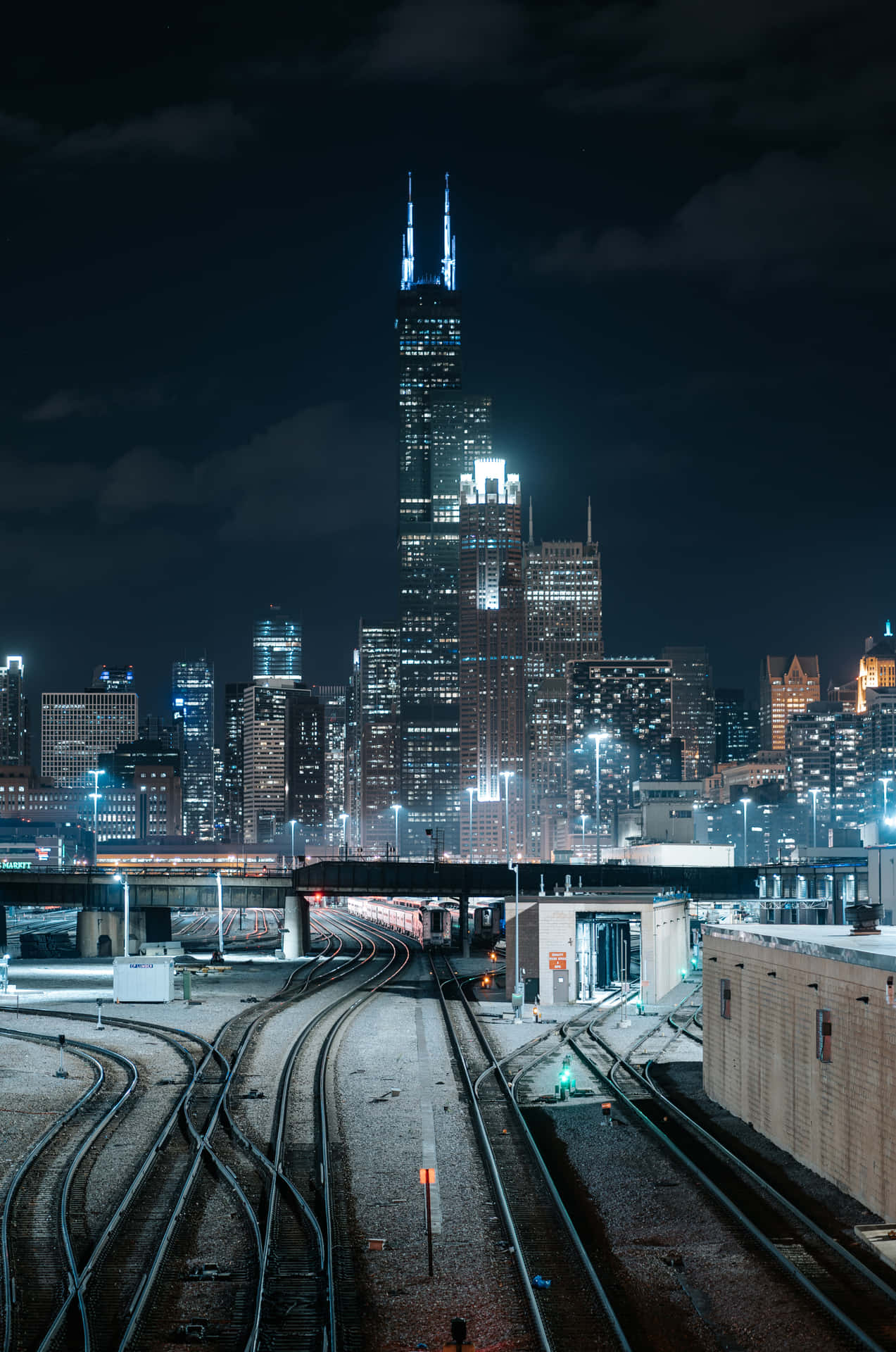 夜晚的城市場景，有發光的摩天大樓和交錯的火車軌道。