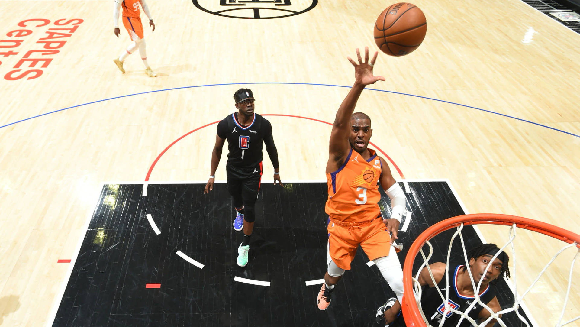 芝加哥太陽隊 NBA 得分瞬間 壁紙 — 一名身穿橙色球衣的籃球運動員跳向籃框，球舉過頭頂，防守球員從下方觀看。