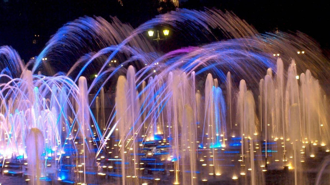 色彩繽紛的發光噴泉水柱在夜間城市廣場上優雅地劃出弧線。