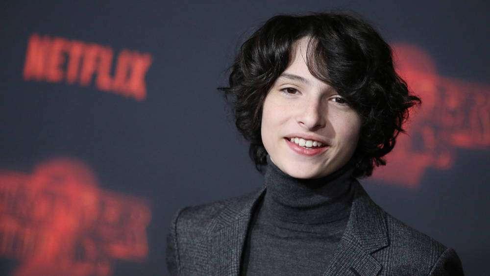 年輕人在Netflix活動中穿著灰色高領毛衣和西裝外套對著鏡頭微笑。