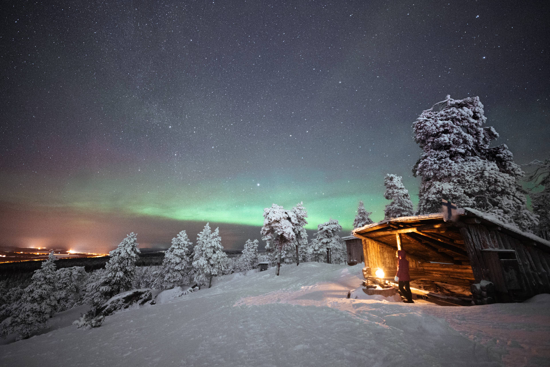 夜晚在北極光下站在雪覆蓋的小屋中的人