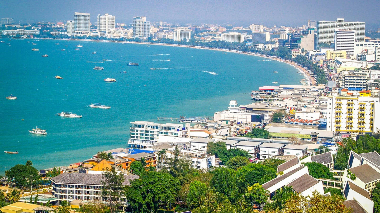 芭堤雅市臨海全景 壁紙 — 繁忙海岸城市的鳥瞰圖，碧綠海水點綴著船隻，密集的城市天際線在晴朗天空下展現。