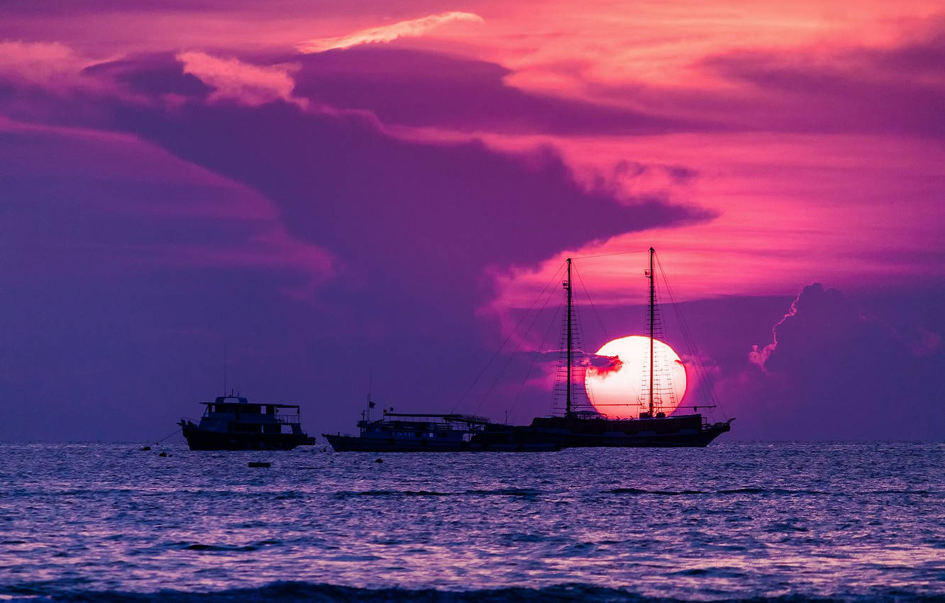 芭堤雅粉紫夕陽 壁紙 — 剪影船隻在平靜的水面上，背景是戲劇性的粉紅和紫色日落天空。