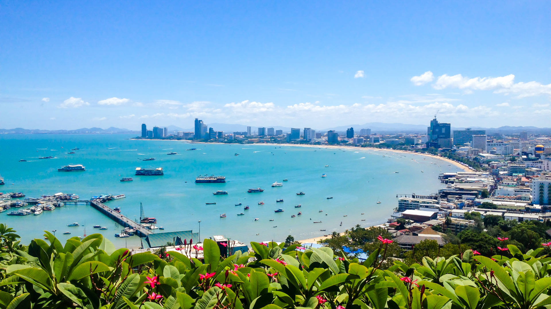 芭堤雅蔚藍海景 壁紙 — 充滿活力的沿海城市景觀，碧綠的海水點綴著船隻，沙灘在明亮的藍天下蜿蜒。