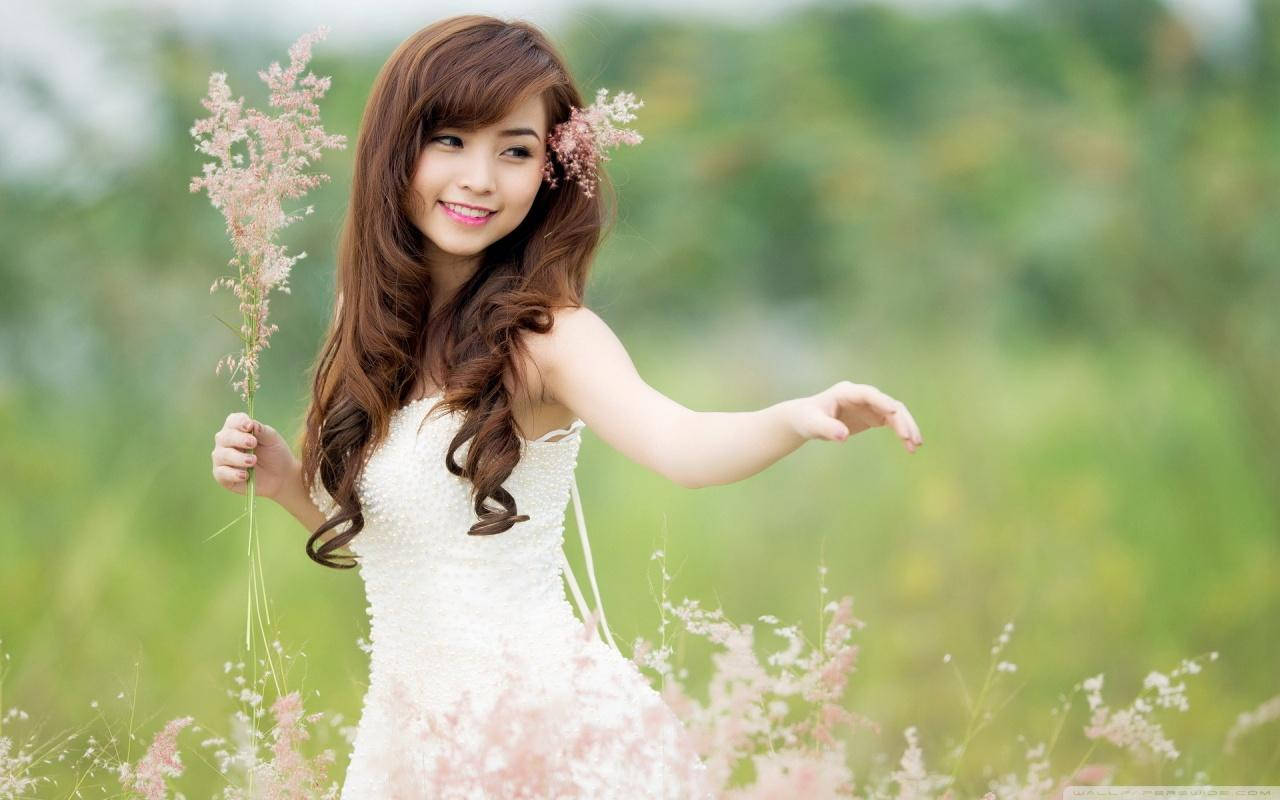 年輕女子穿著白色連衣裙在陽光明媚的草地上手持粉紅色的草。