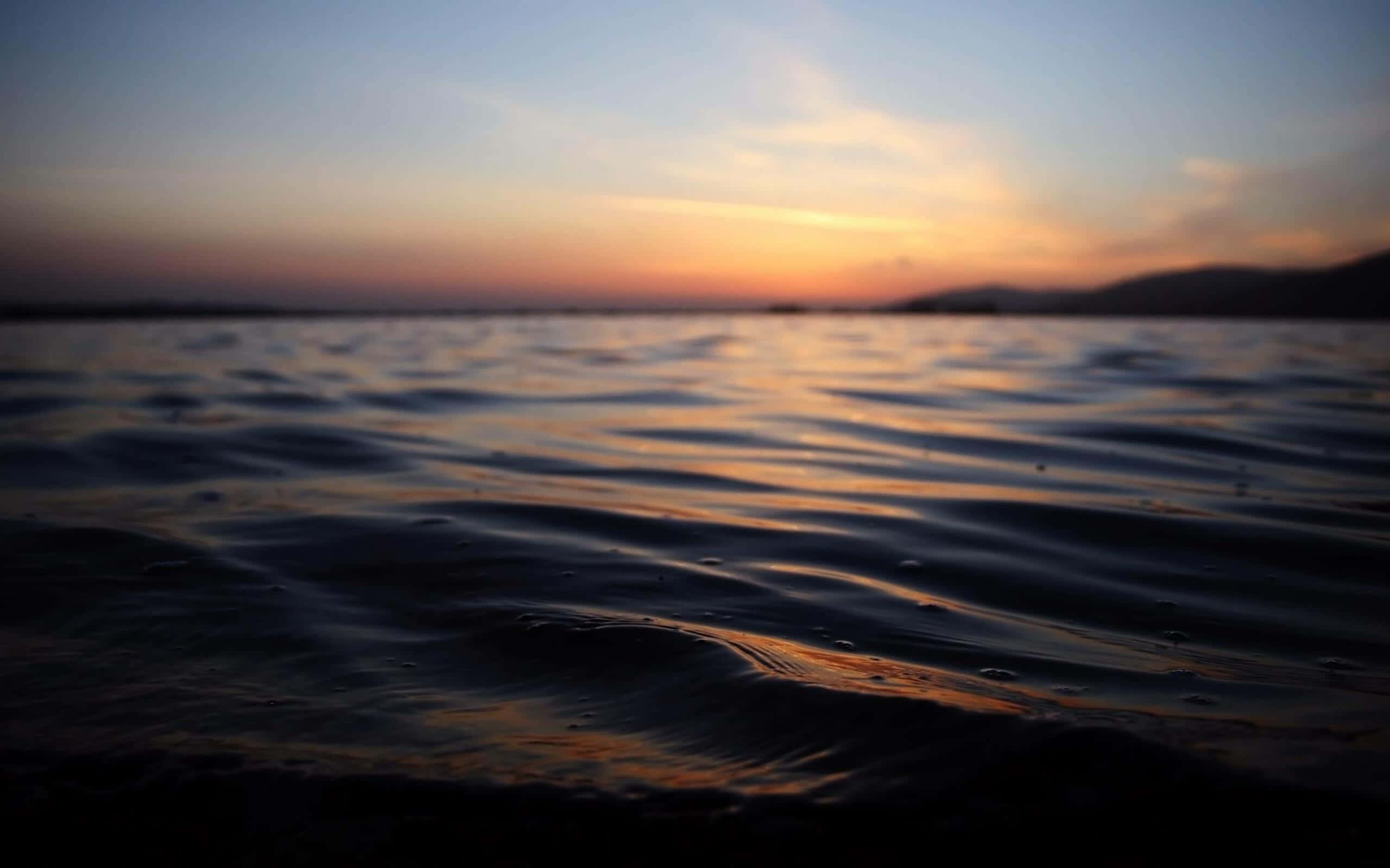 花點時間放鬆與深呼吸 壁紙 — 夕陽以溫暖色調塗抹天空，倒映在漣漪的水面上，遠山在漸暗的光線中呈現剪影。