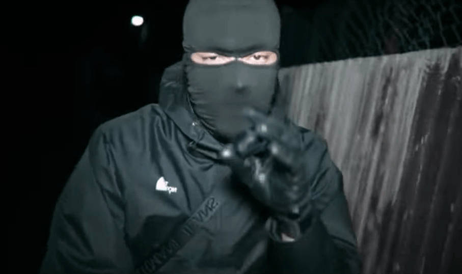 一個穿黑色衫嘅蒙面人喺夜晚用槍指向觀眾。