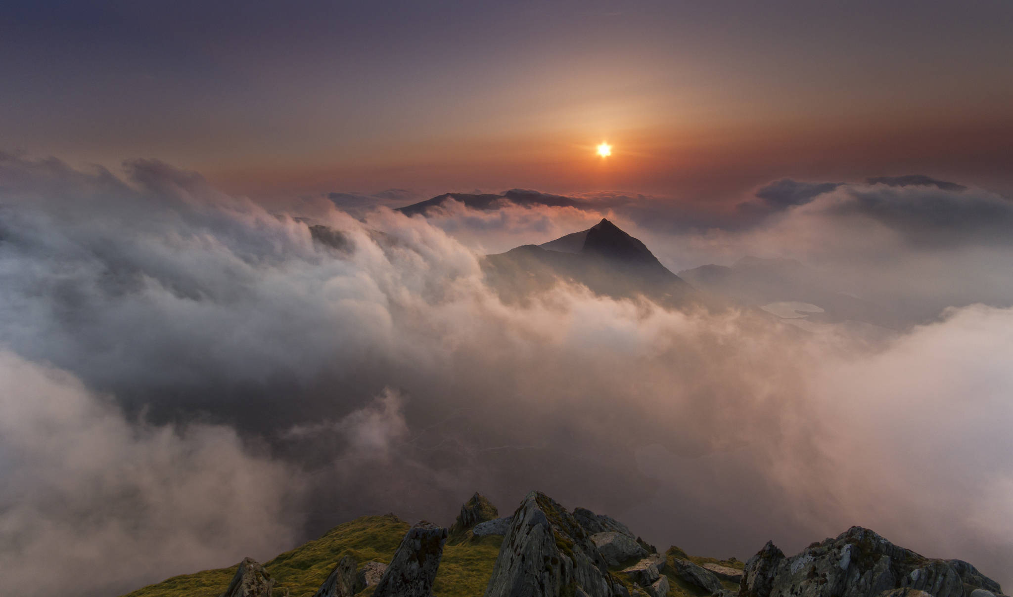 英國南特格溫安特山谷 壁紙 — 山峰穿透雲海，太陽以溫暖的橙色和紫色色調升起。
