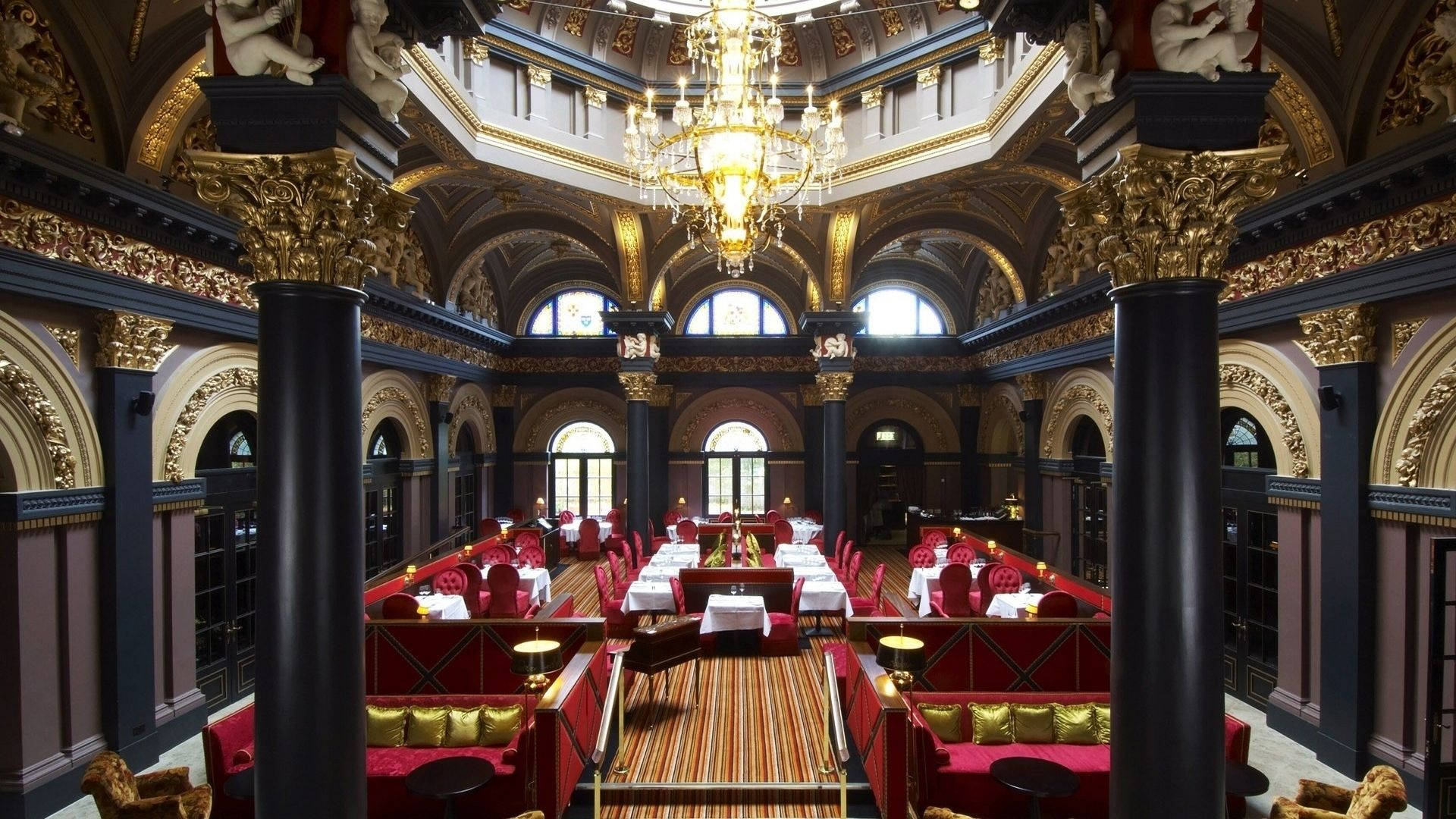 英國商旅酒店內的餐廳 壁紙 — 宏偉華麗的餐廳，拱形天花板下設有鍍金柱子、吊燈和紅色天鵝絨座椅。