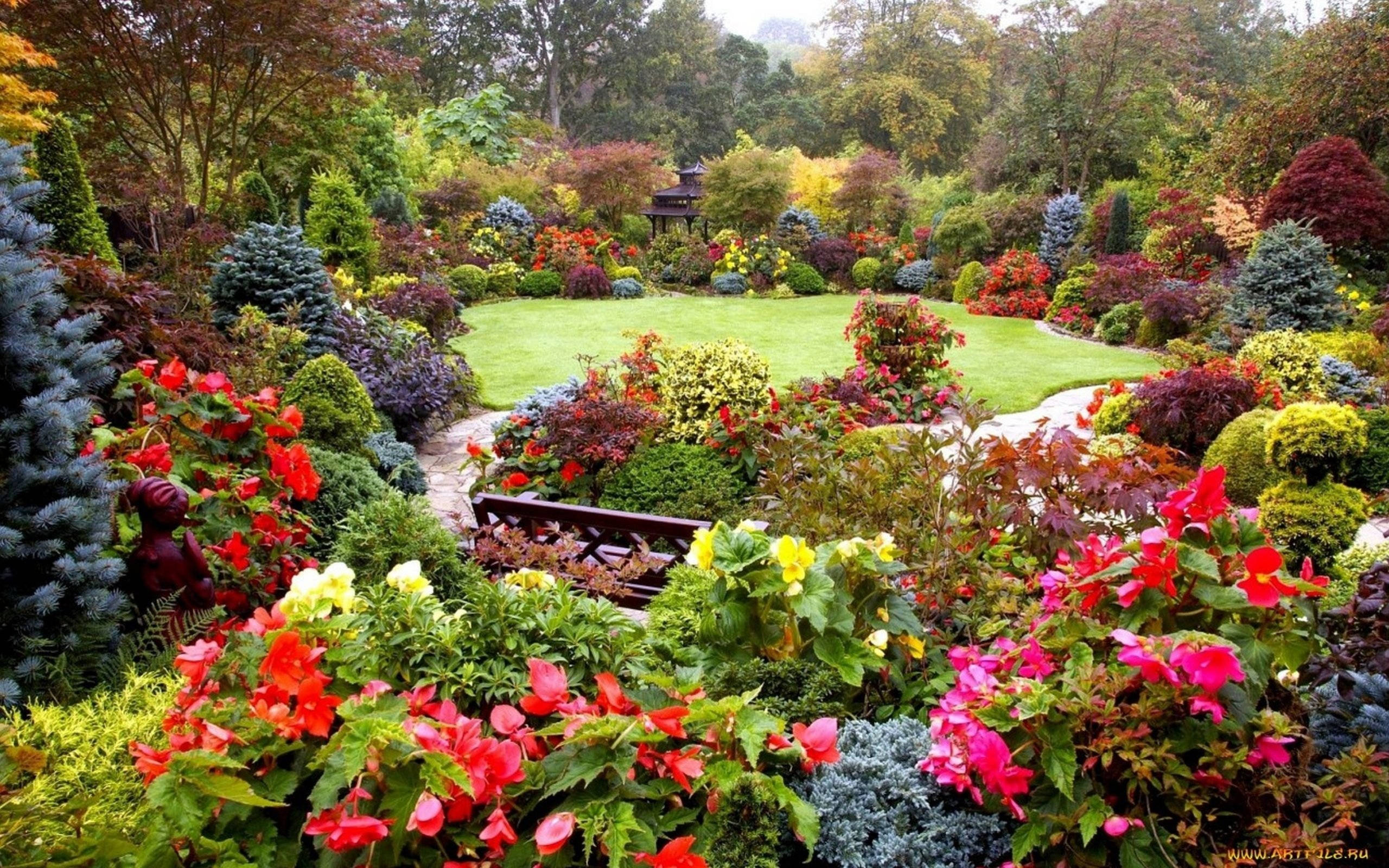 英國四季花園春日美景 壁紙 — 一個充滿活力的花園，開滿了紅色、粉紅色和黃色的花朵，蜿蜒環繞著一條石徑，通往草地和遠處的涼亭。