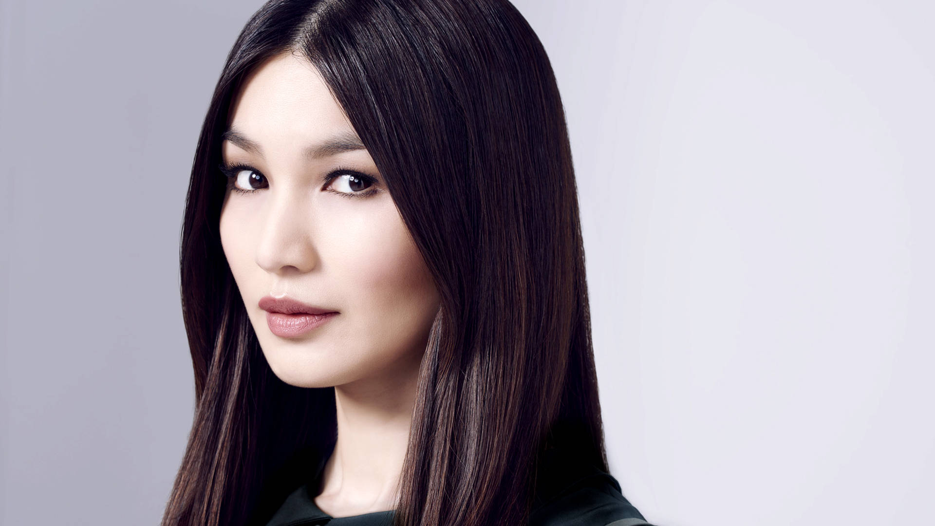 英國女演員 Gemma Chan 壁紙 — 一位長黑髮的女性在工作室肖像中，對著純灰色背景柔和地凝視。