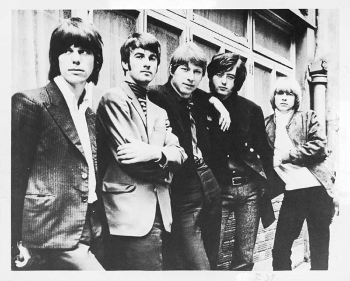 英國搖滾樂團 The Yardbirds 黑白影像 壁紙 — 五位穿著1960年代時尚的年輕男性，在一棟風化的建築外牆前自信地擺姿勢，拍攝成一張經典黑白照片。