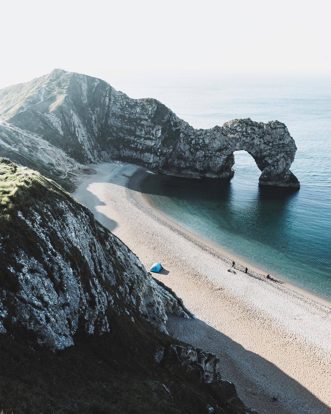 英國杜德爾門海灘 壁紙 — 從高空俯瞰杜德爾門天然石灰岩拱門，下方有藍色帳篷、碧綠海水和沙灘。