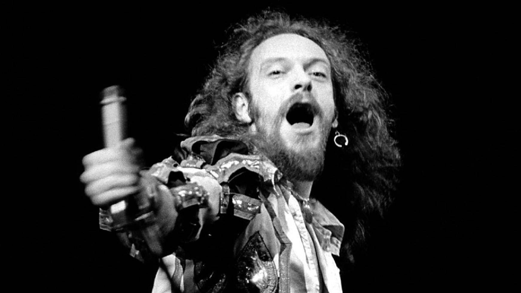 英國歌手伊恩·安德森 Jethro Tull 樂隊單色肖像 壁紙 — 一個鬍鬚搖滾歌手，頭髮狂野，在舞台上對著咪高峰尖叫的黑白特寫。