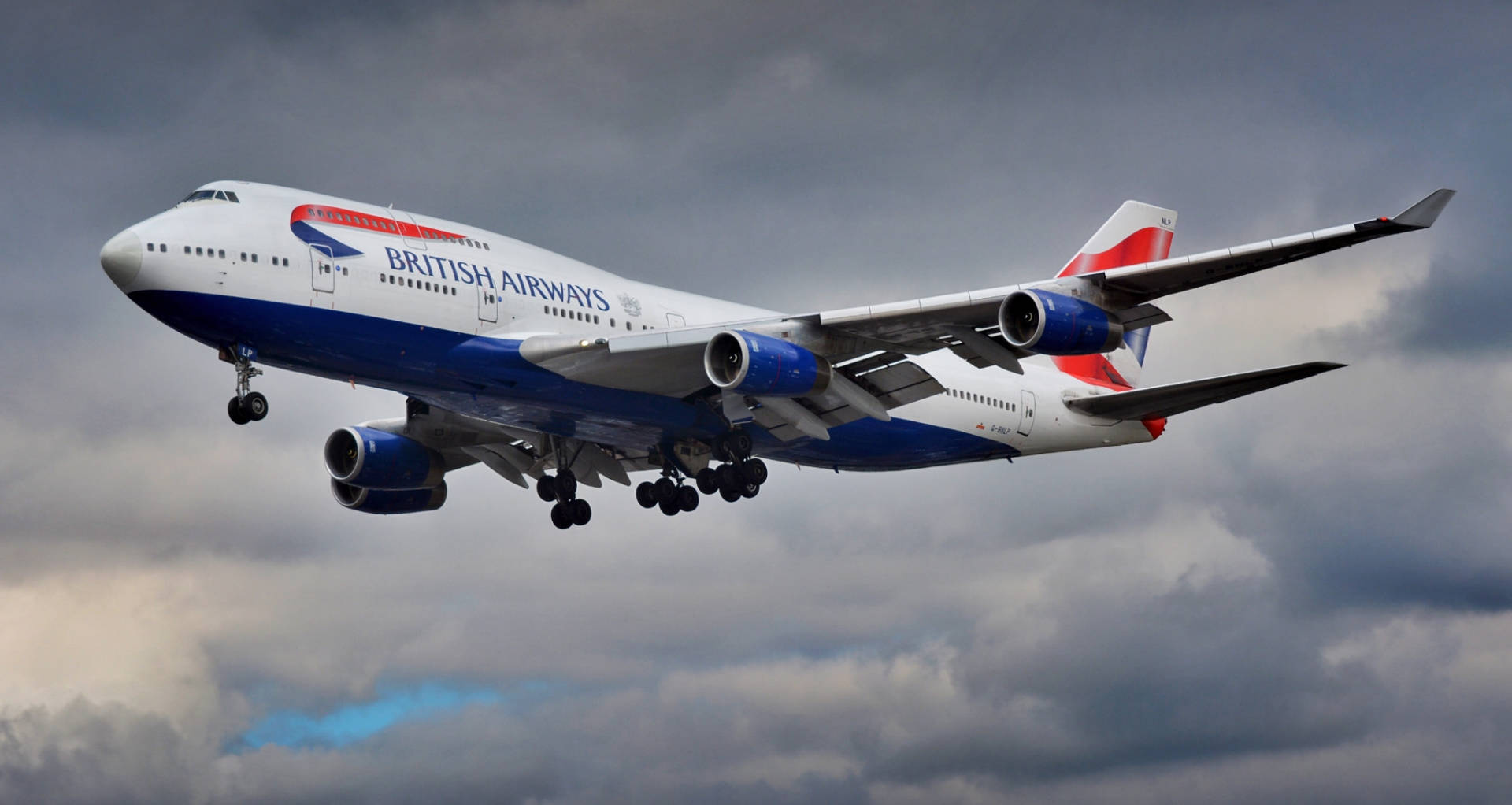 英國航空珍寶客機低飛，起落架伸出，映襯多雲天空。
