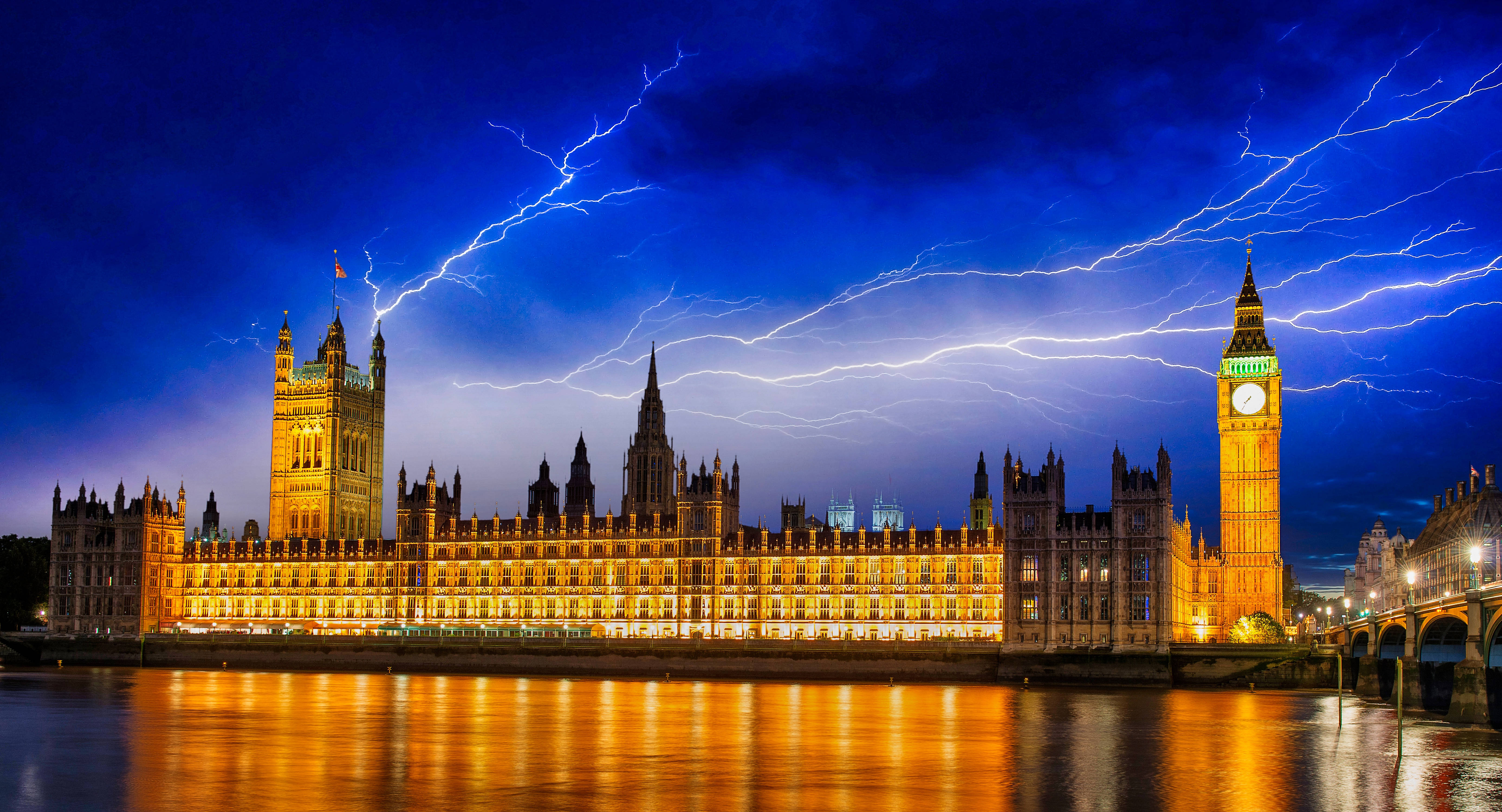 英國議會大廈 壁紙 — 倫敦標誌性的國會大廈和大本鐘在佈滿閃電的戲劇性天空下溫暖地發光。