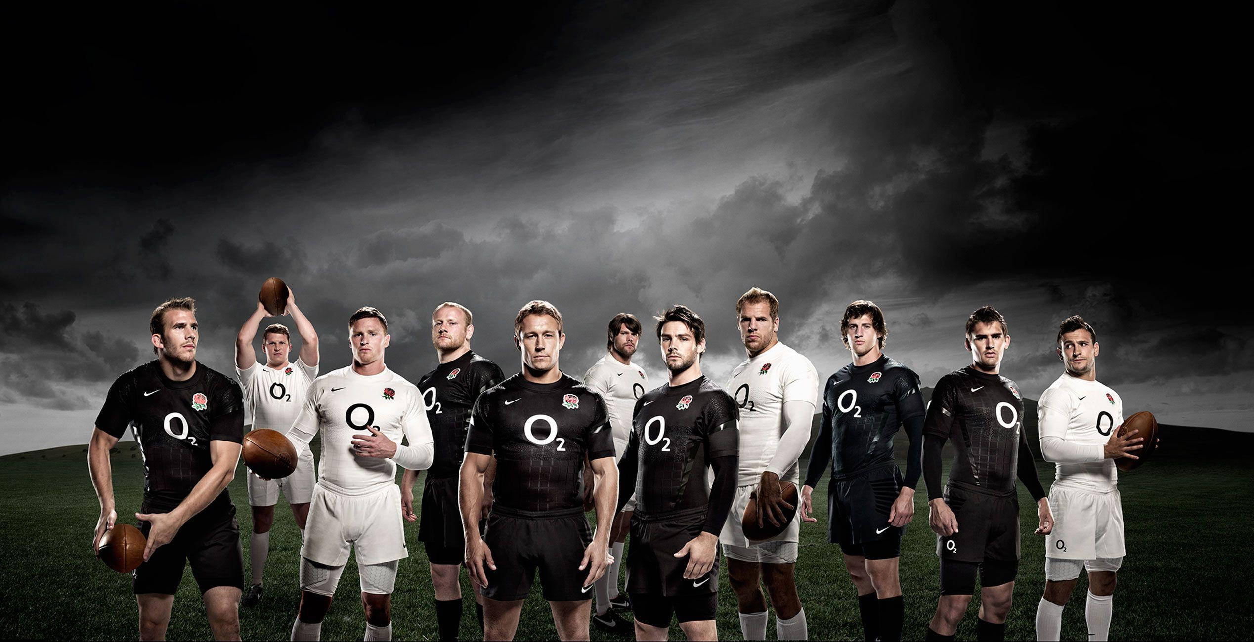 英格蘭rugby 攝影 壁紙 — 一支穿著黑白球衣的欖球隊在戲劇性的暴風雨天空下自信地站在草地上。