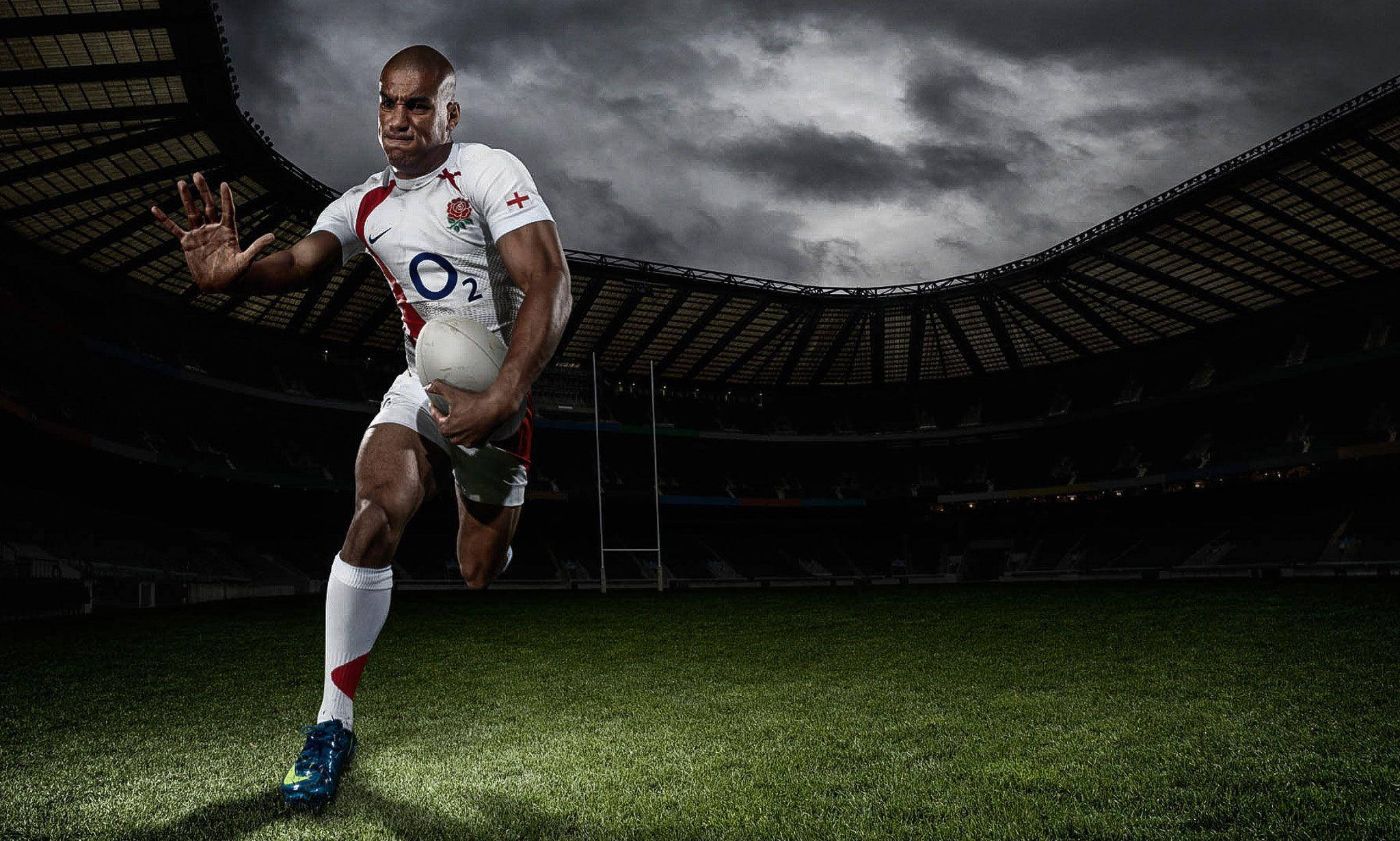 英格蘭國家rugby攝影 壁紙 — 一名身穿白色球衣的欖球運動員在戲劇性的暴風雲下持球衝過球場。
