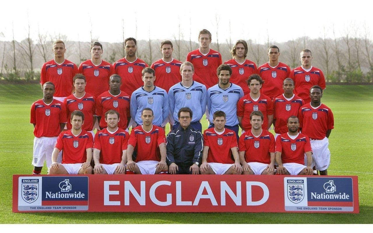 England 桌布 壁紙 — 英格蘭國家足球隊在草地上正式擺姿勢，身穿紅色球衣，背景有光禿禿的樹木。
