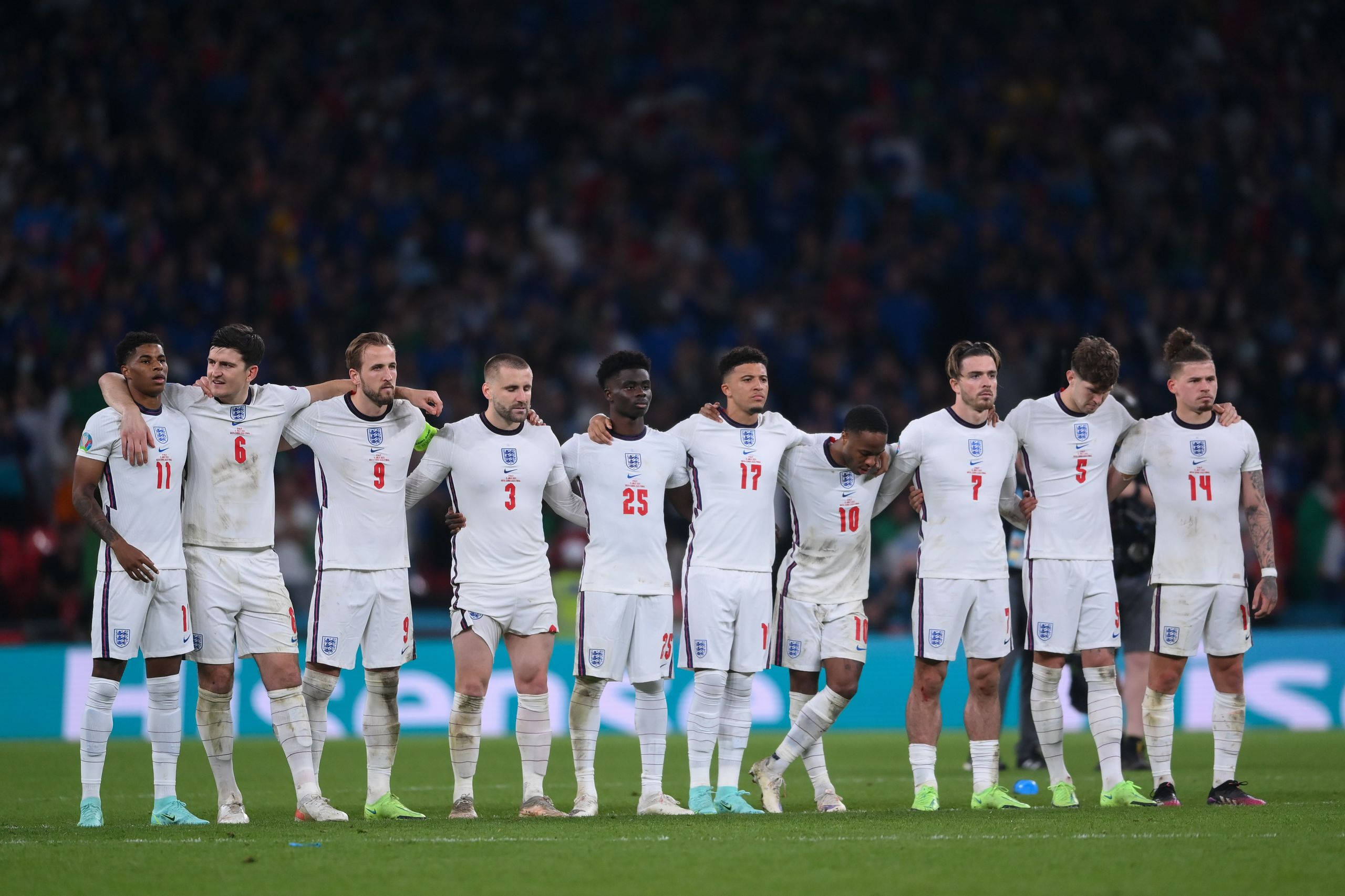 Football Players 桌布 壁紙 — 英格蘭足球隊在球場上肩並肩站立，在明亮的燈光下低頭肅穆團結。