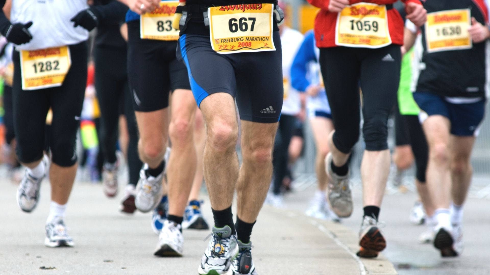 英聯邦運動會馬拉松比賽 壁紙 — 馬拉松跑手雙腳在鋪砌街道上移動的特寫，可見比賽號碼布。