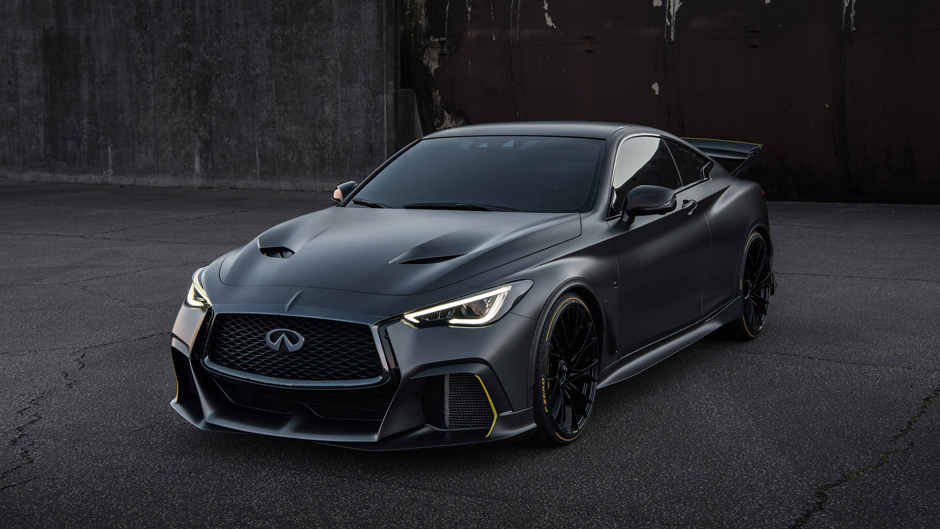 英菲尼迪 Project Black S 壁紙 — 一輛帶有黃色點綴的啞光黑色 Infiniti 跑車，停在裂開的瀝青路面上，背景是風化的混凝土牆。