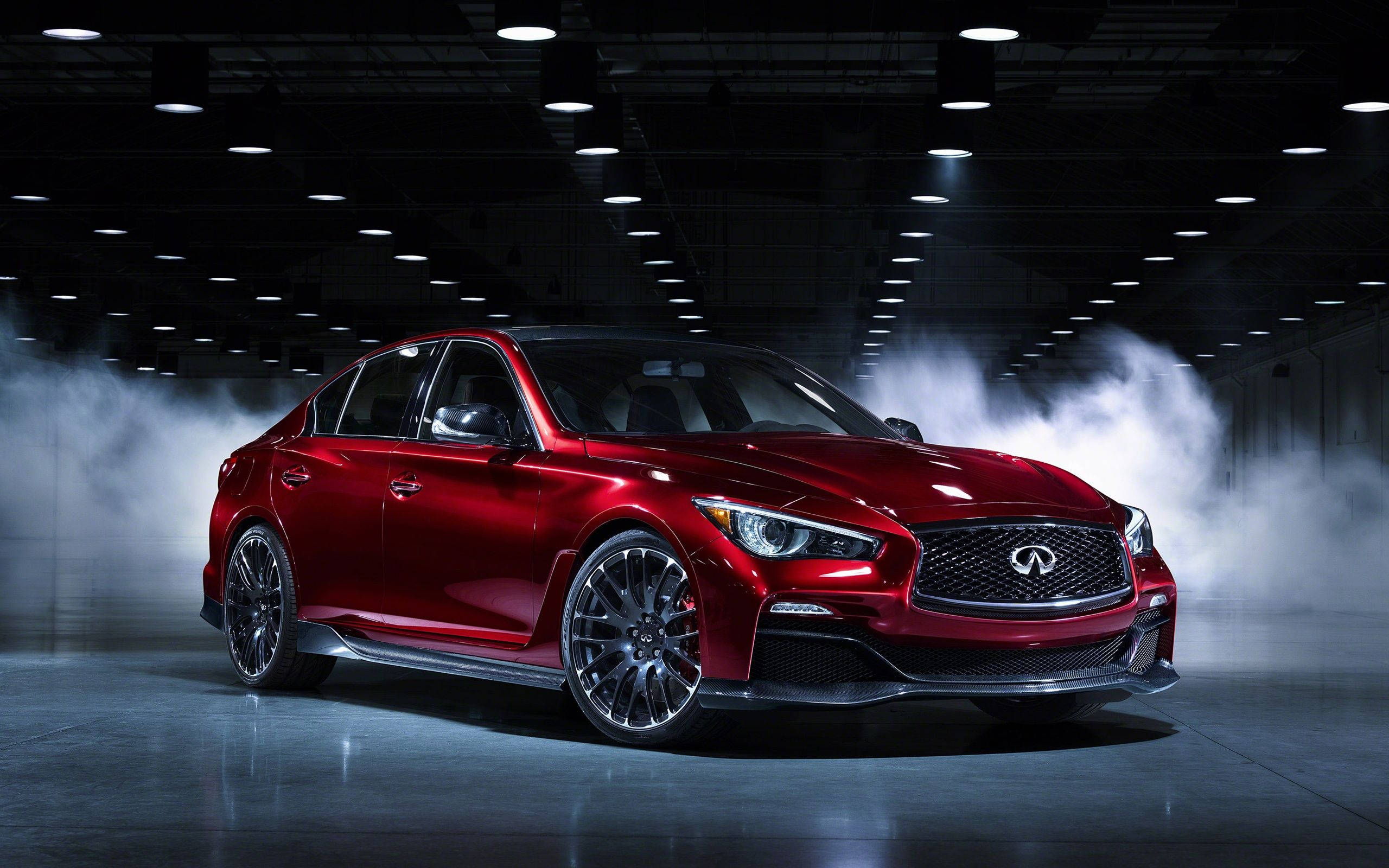 英菲尼迪 Q50 Eau Rouge 壁紙 — 一輛光亮的紅色 Infiniti 房車在黑暗的工業機庫中，於旋轉的煙霧中在攝影棚燈光下閃閃發光。