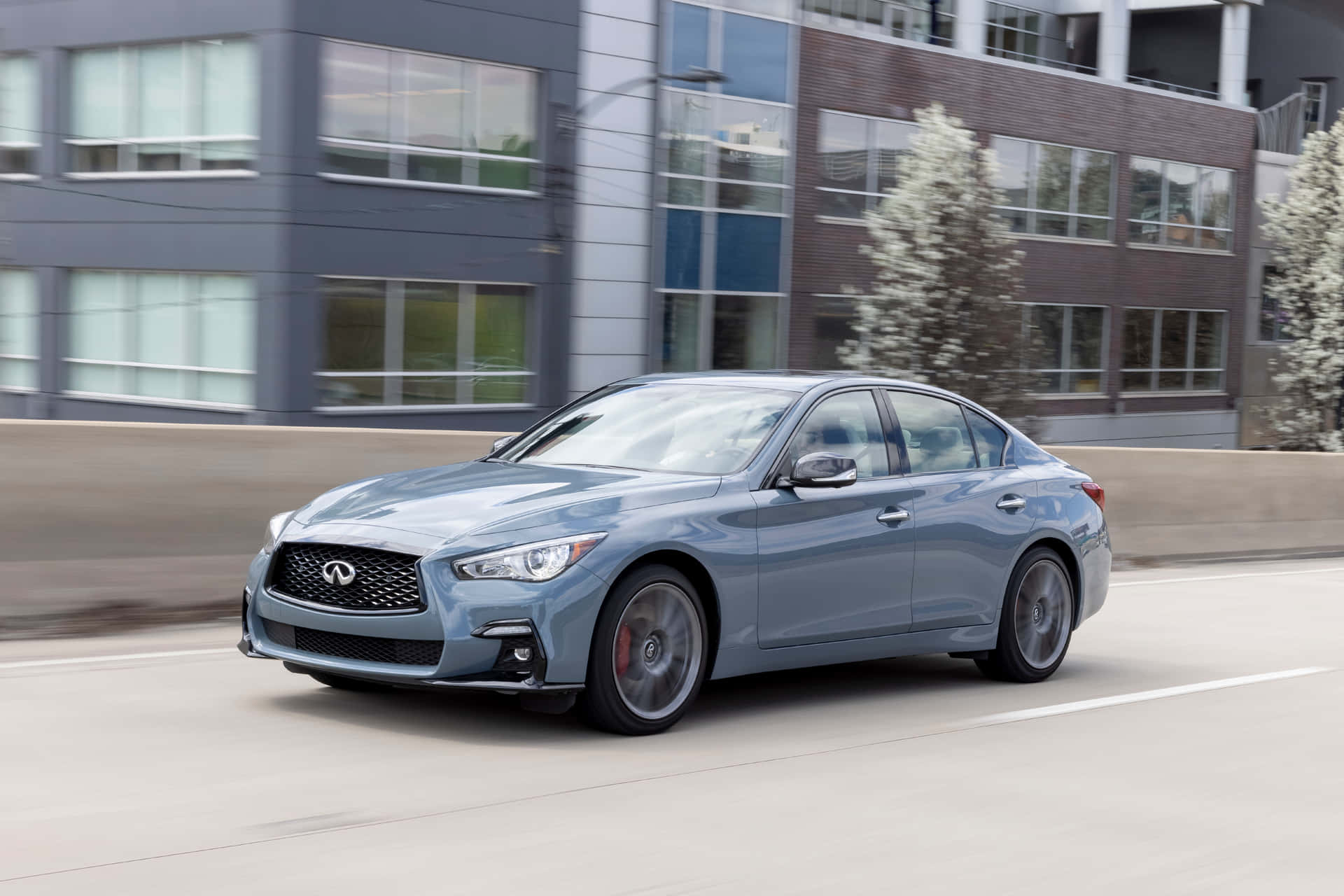 銀色 Infiniti 房車在城市街道上行駛，經過現代建築和樹木。