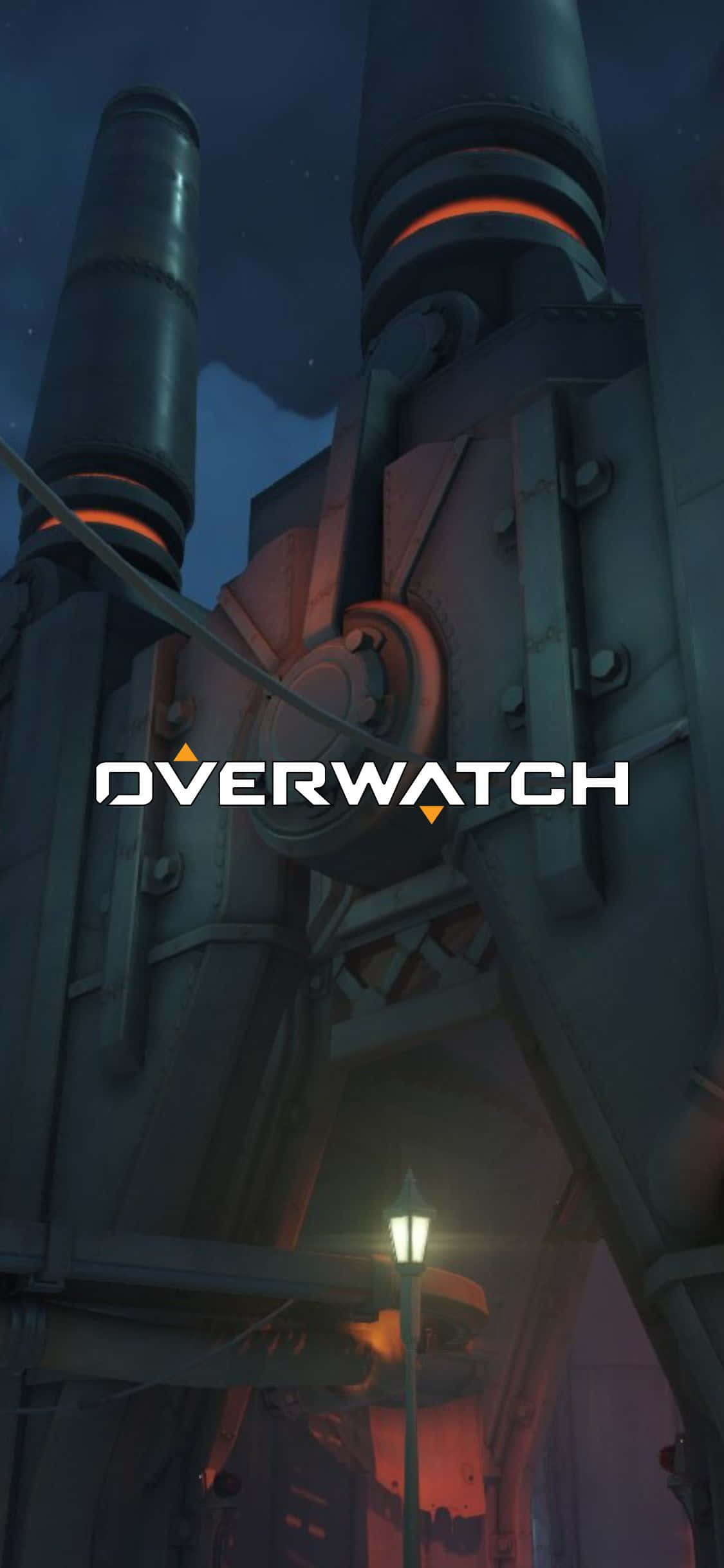 「英雄永不死」— 在 iPhone X 上體驗《Overwatch》的精彩世界 壁紙 — 一座高聳的機械結構在黑暗的夜空下發出橙色光芒，下方有一盞路燈。
